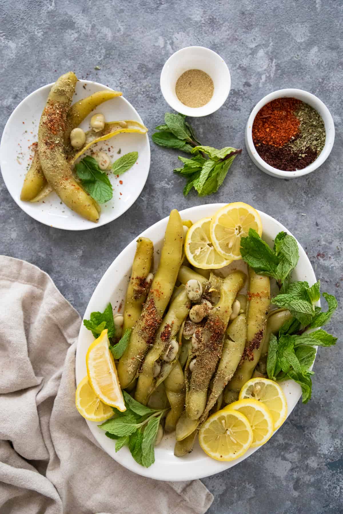 Broad beans on a grey background on a plate and platter with spices, mint and lemon. 