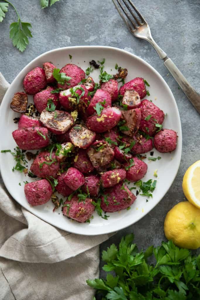 overhead shot of roasted radishes on a white plate on a grey backdrop.