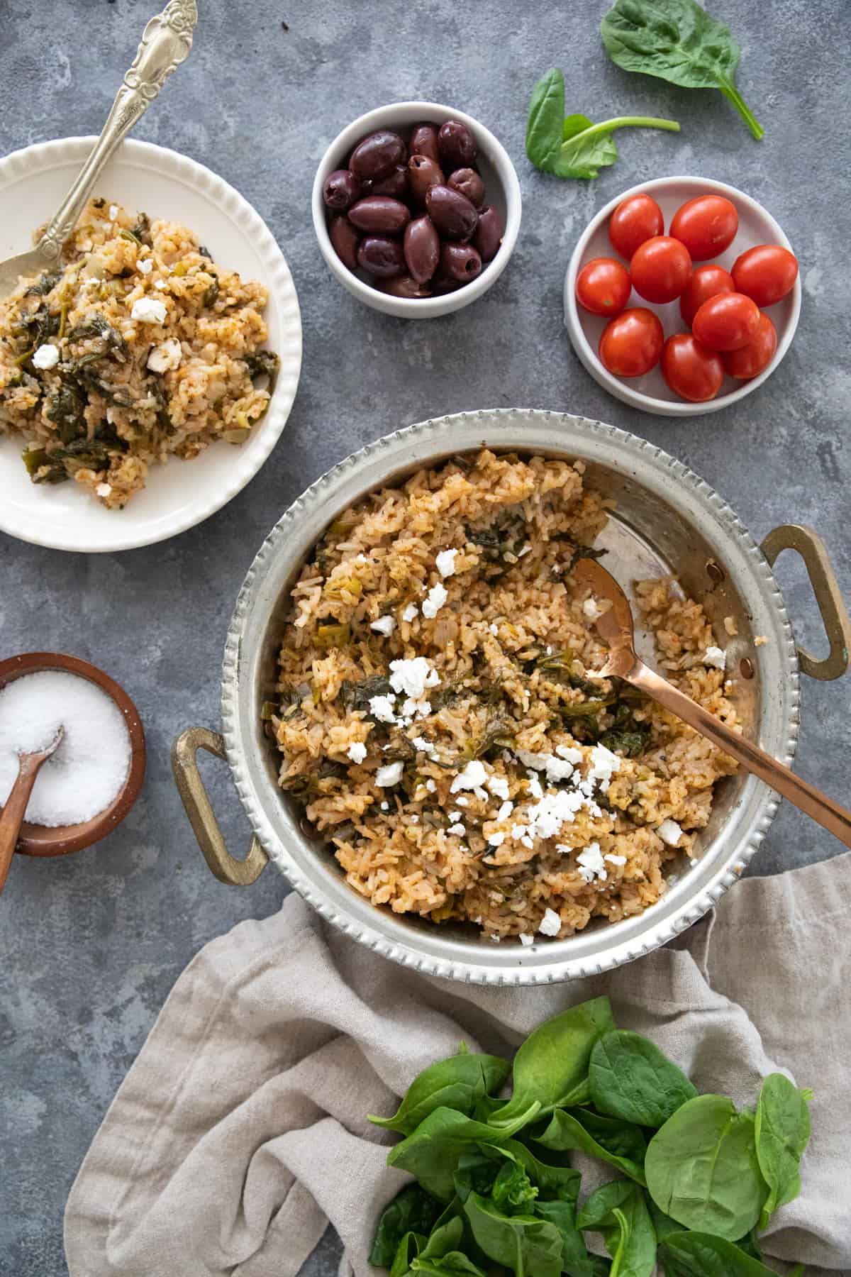A pan or Greek spinach rice and a plate with a side of tomatoes and olives. 