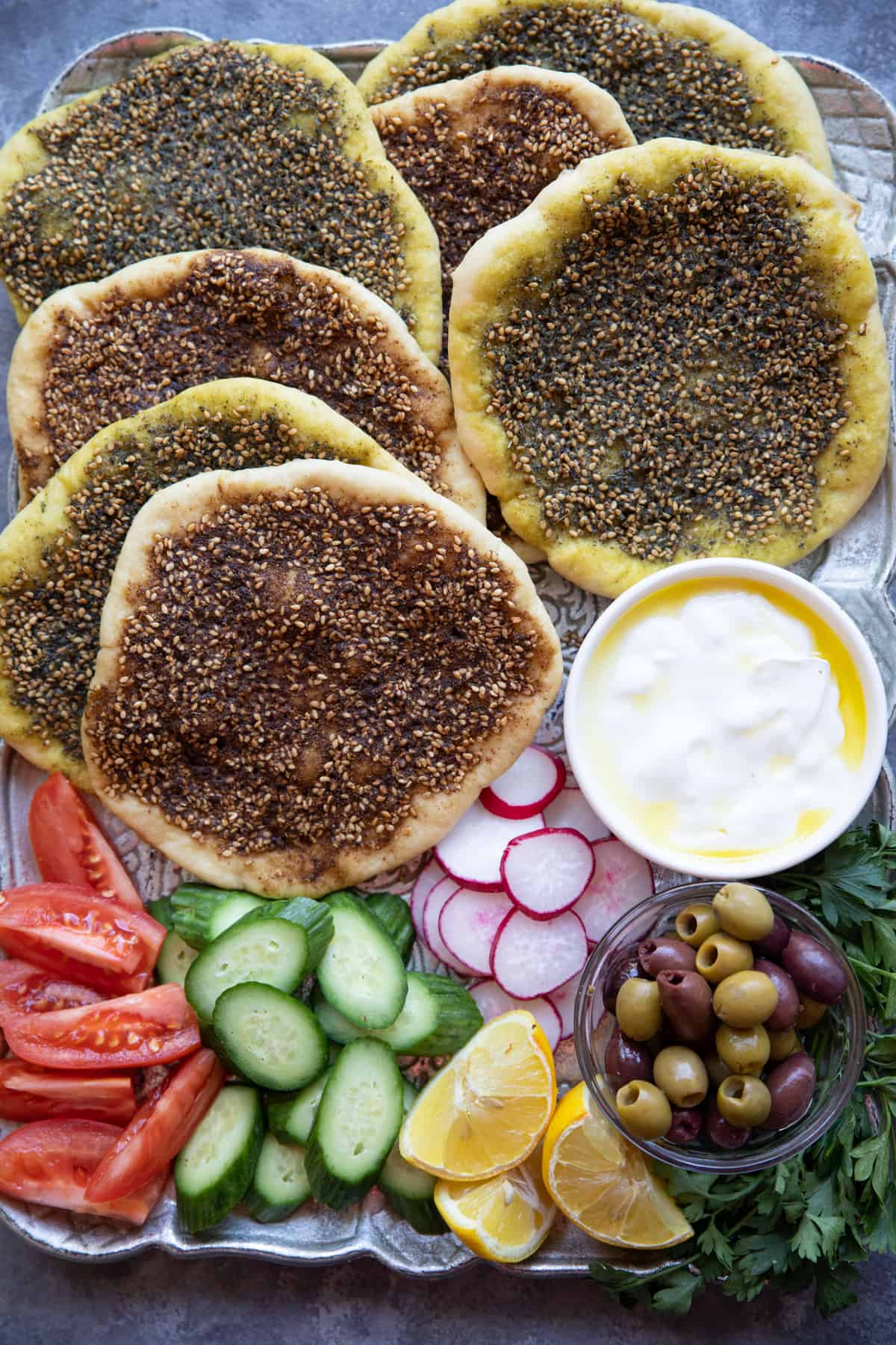 overhead shot of a platter of zaatar bread manakish with vegetables and olives. 