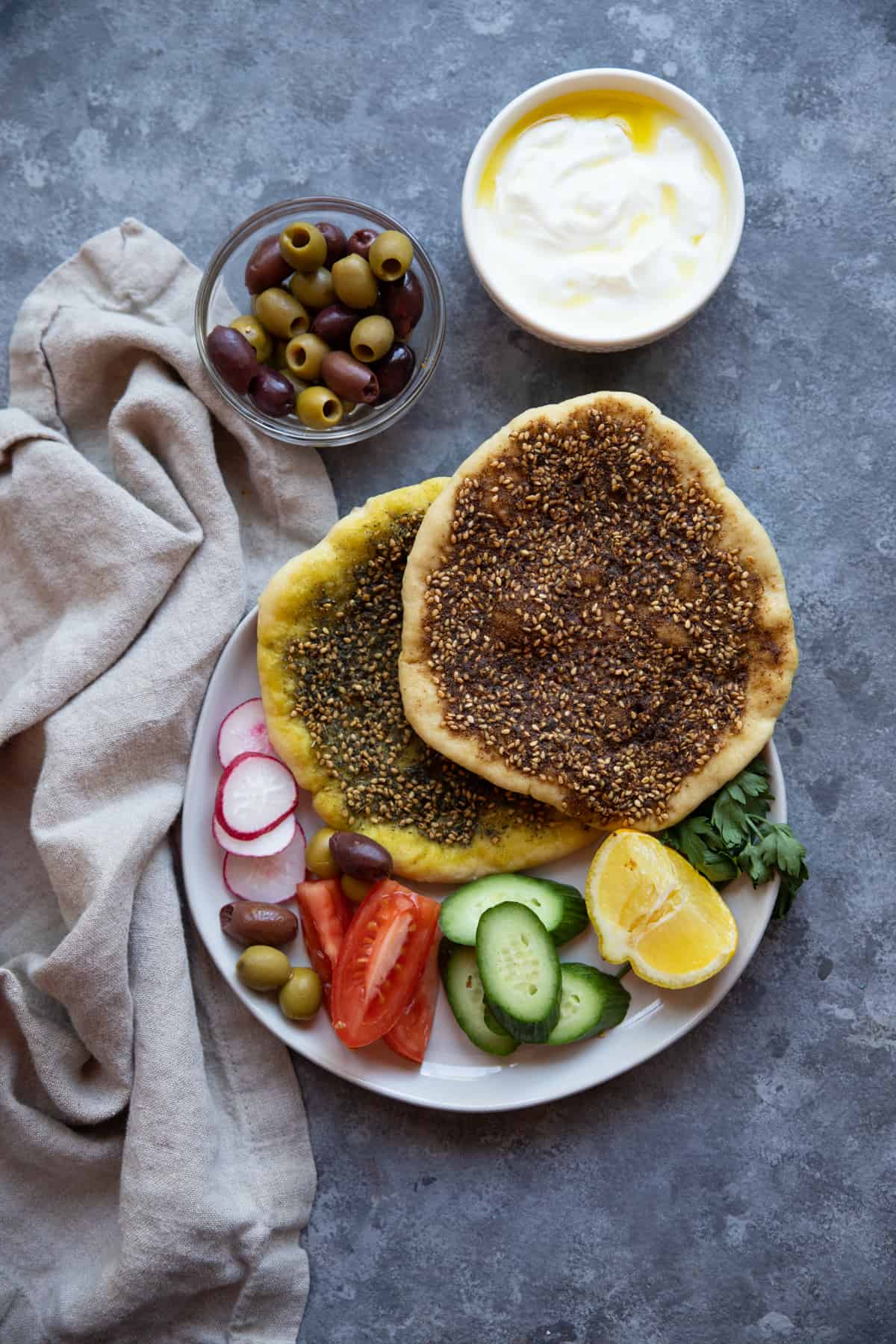 2 manakish zaatar on a plate with vegetables on a grey background. 