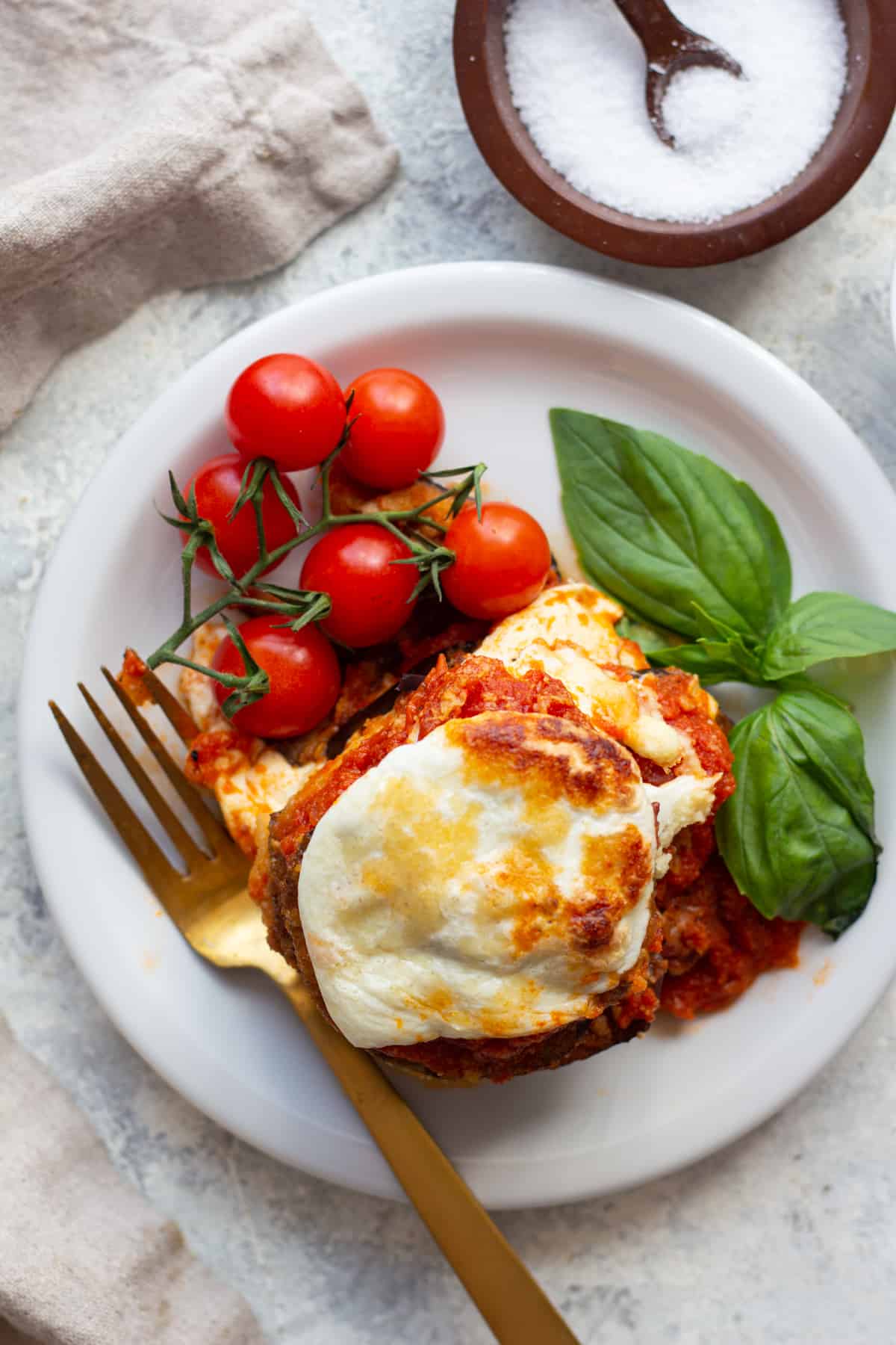 Eggplant parmesan on a plate with basil and tomatoes. 