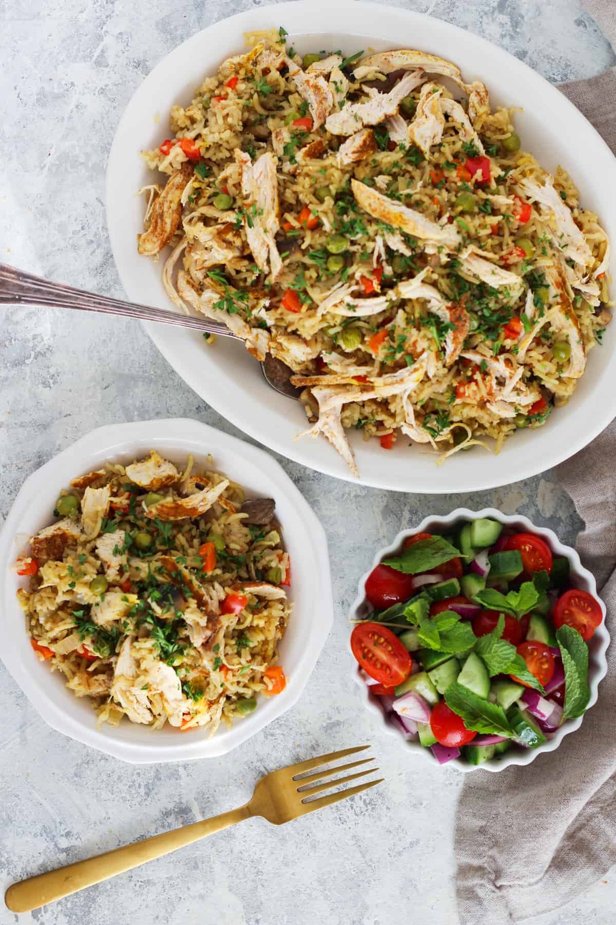 A platter of chicken and rice with vegetables with a serving plate on a white backdrop. 