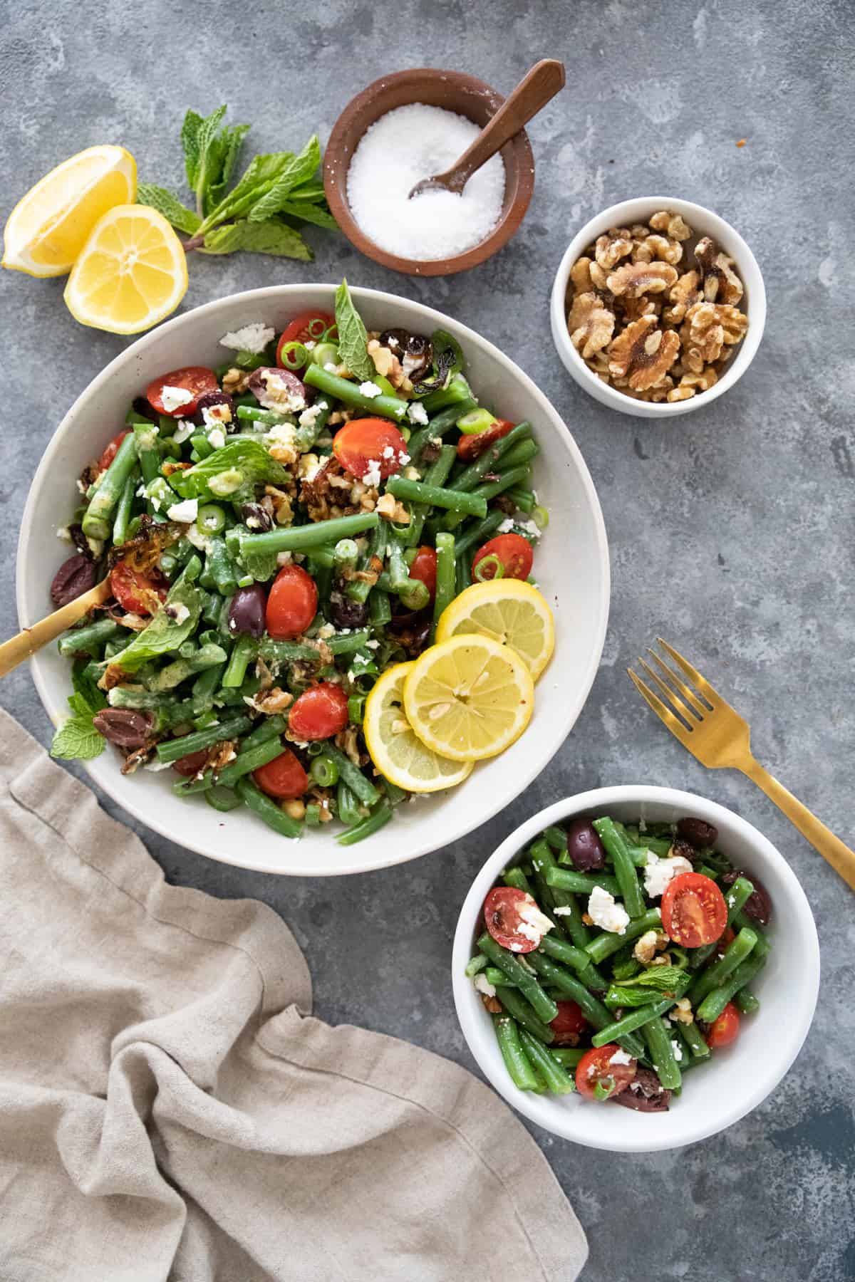 Overhead shot of green bean salad in two different bowls on a grey backdrop. 