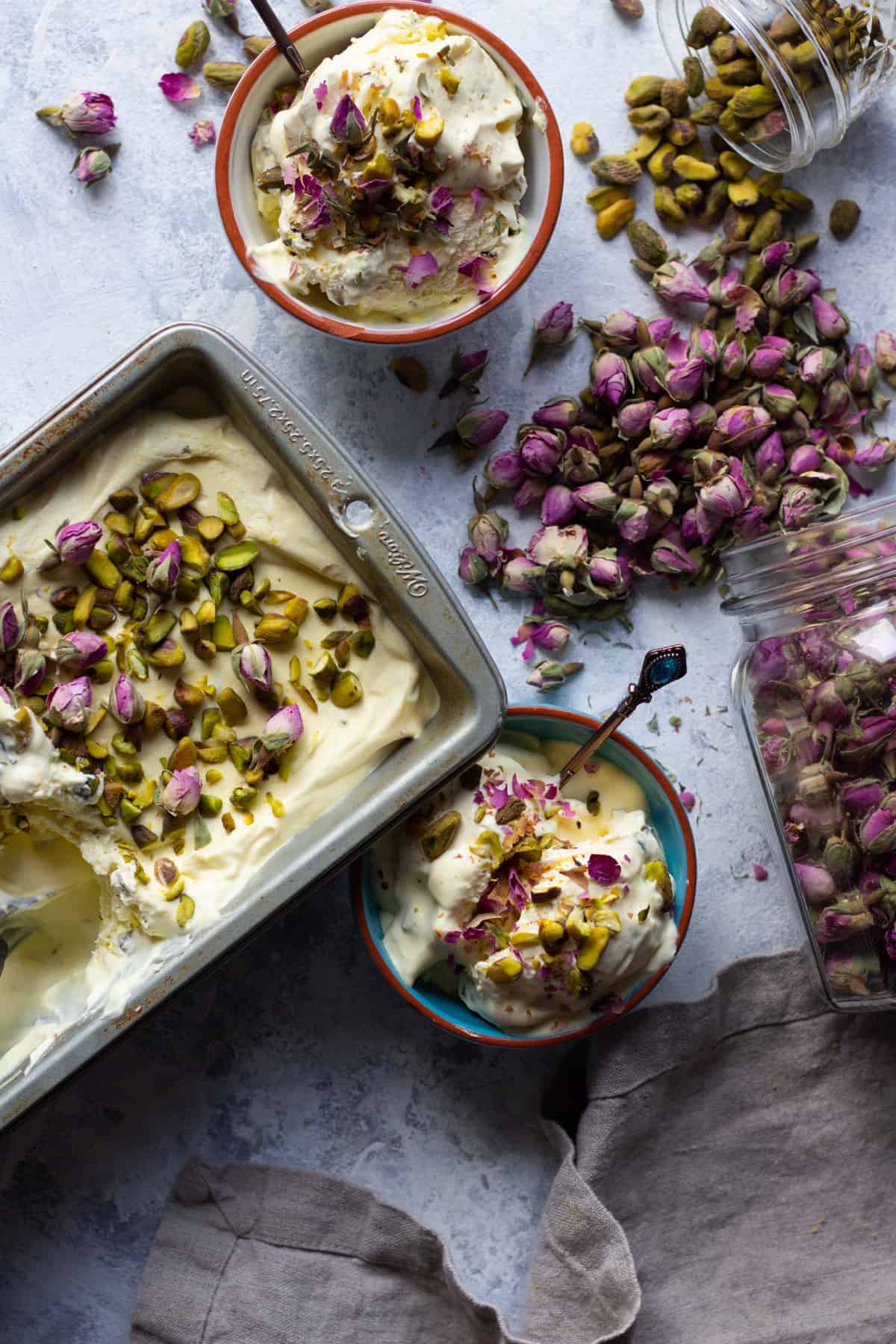 Two bowls of saffron ice cream with a loaf pan full of ice cream topped with pistachios and roses. 