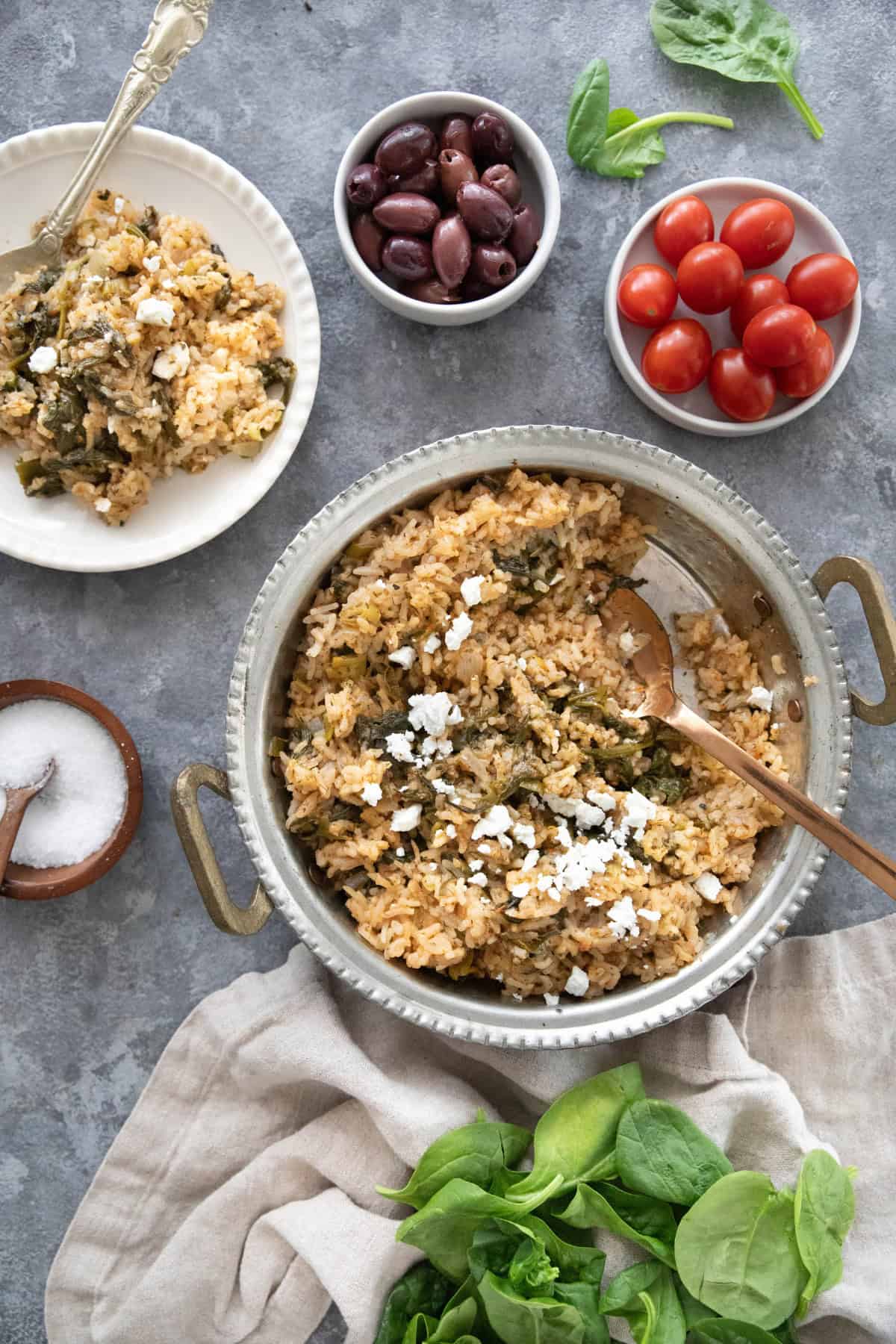 A pan or Greek spinach rice and a plate with a side of tomatoes and olives. 