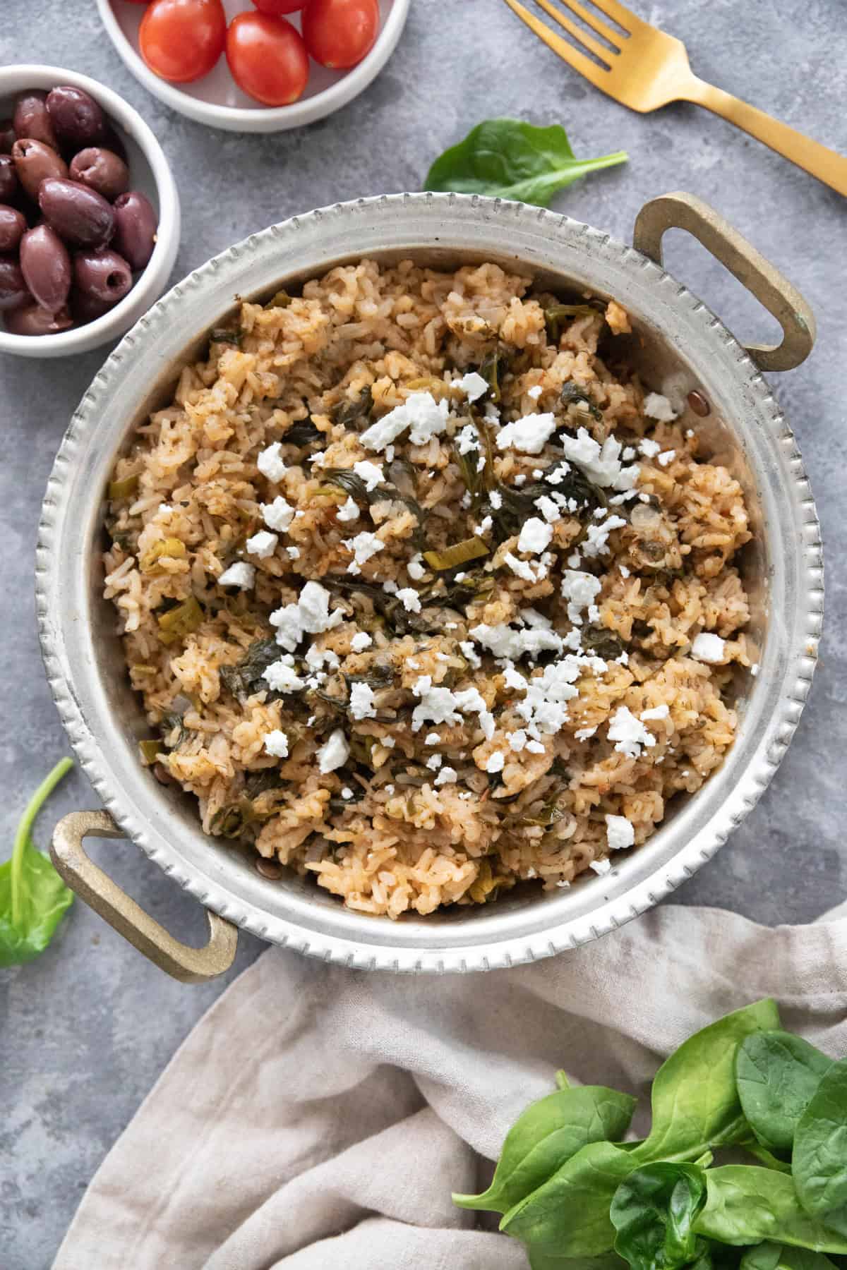 overhead shot of spanakorizo in a pan topped with feta and served with olives and tomatoes. 