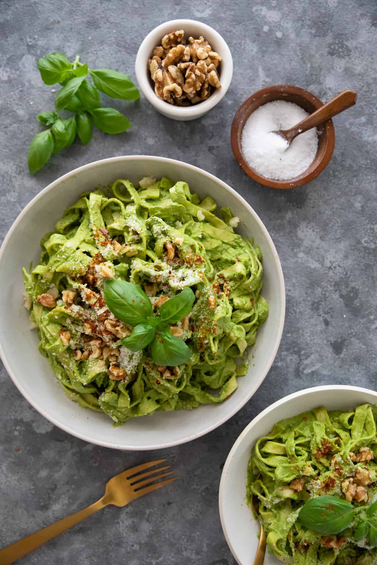 overhead shot of spinach pesto pasta in a bowl on a grey background. 