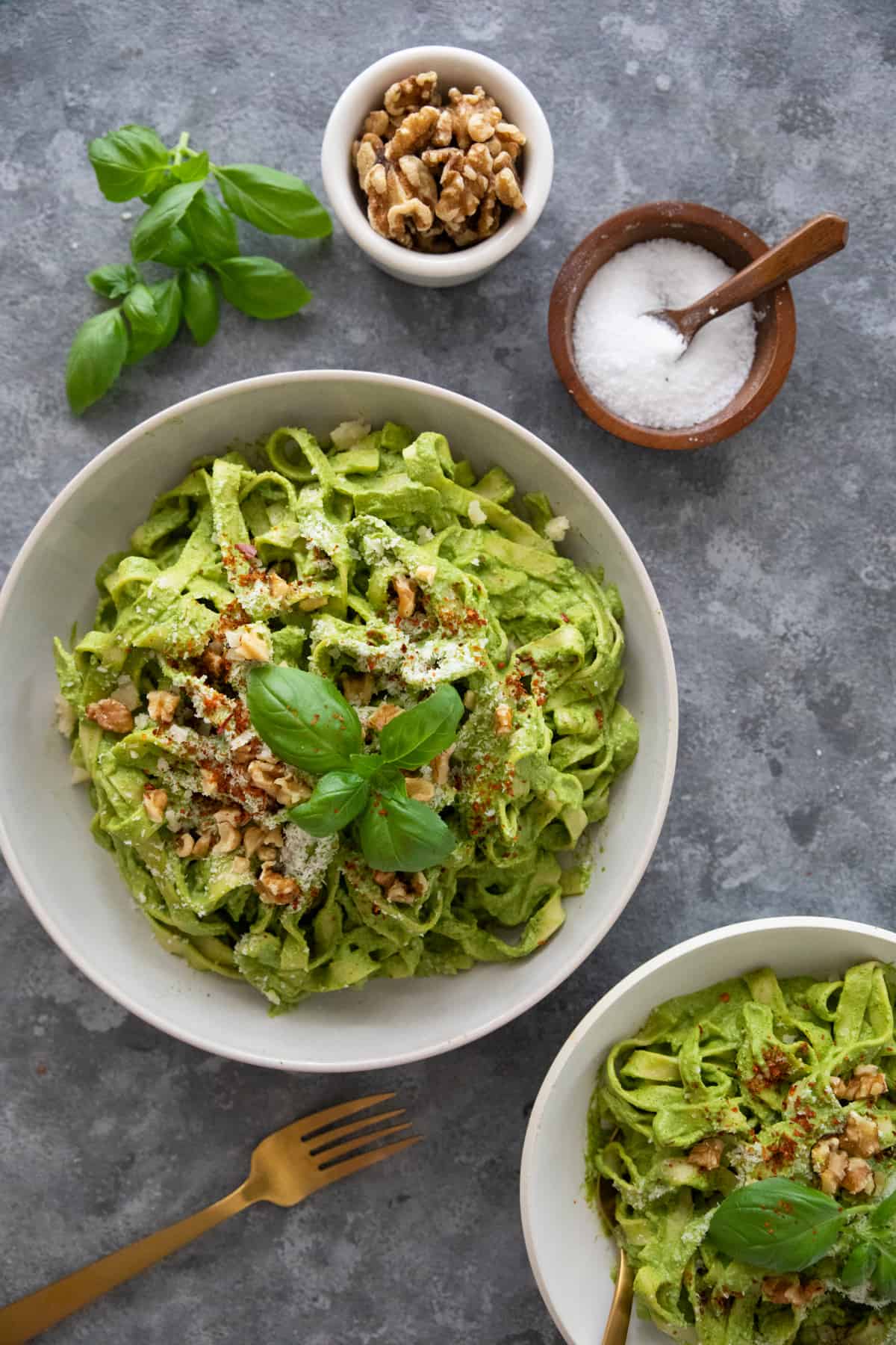 overhead shot of spinach pesto pasta in a bowl on a grey background.