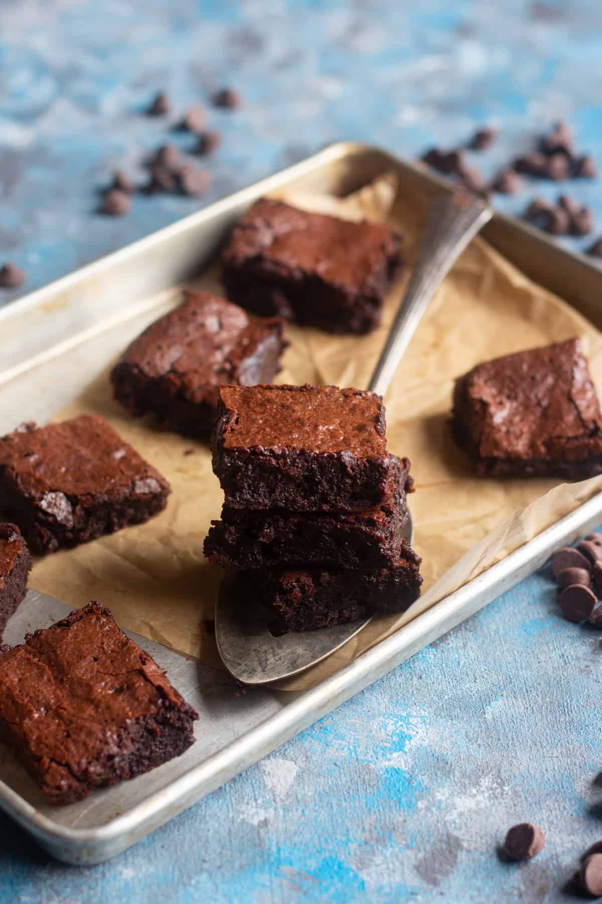 Flourless choclate brownies stacked on a spatula on a baking sheet. 