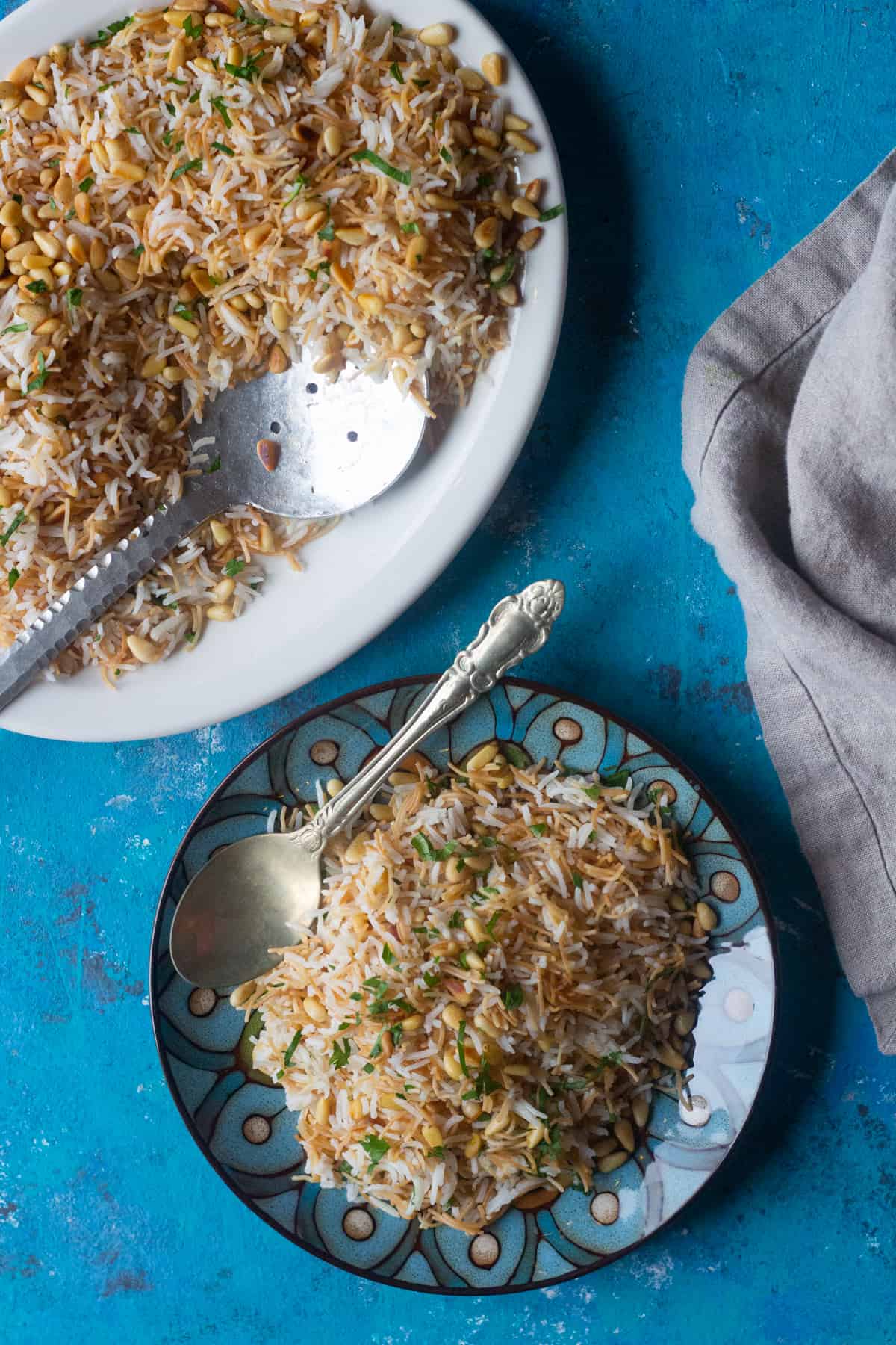 Lebanese pilaf made with rice served on a plate with a spoon and topped with pine nut and parsley. 