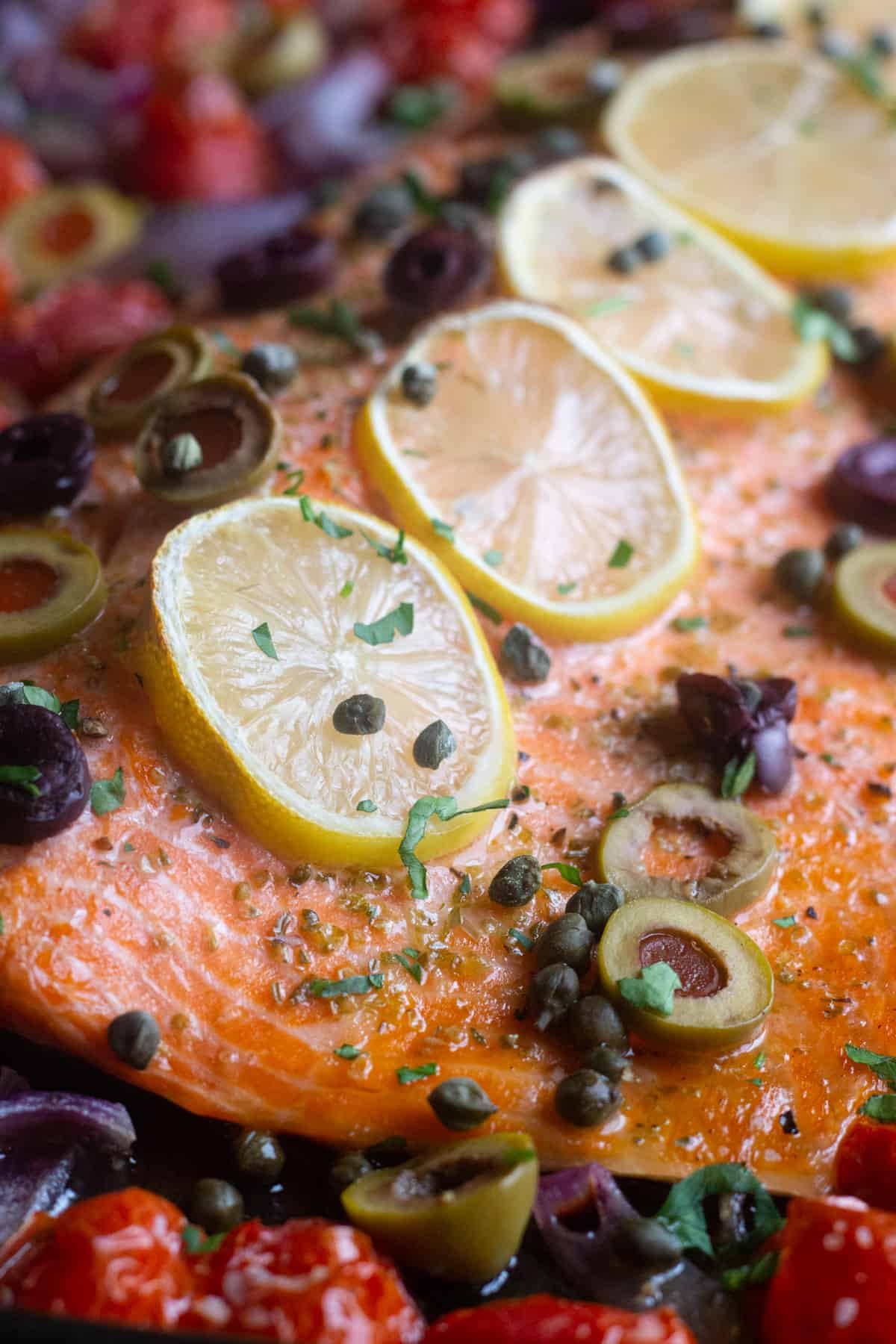 The best ever oven baked salmon is here! Flaky and moist Alaska salmon with olives and capers on a bed of vegetables is the best weeknight dinner!
