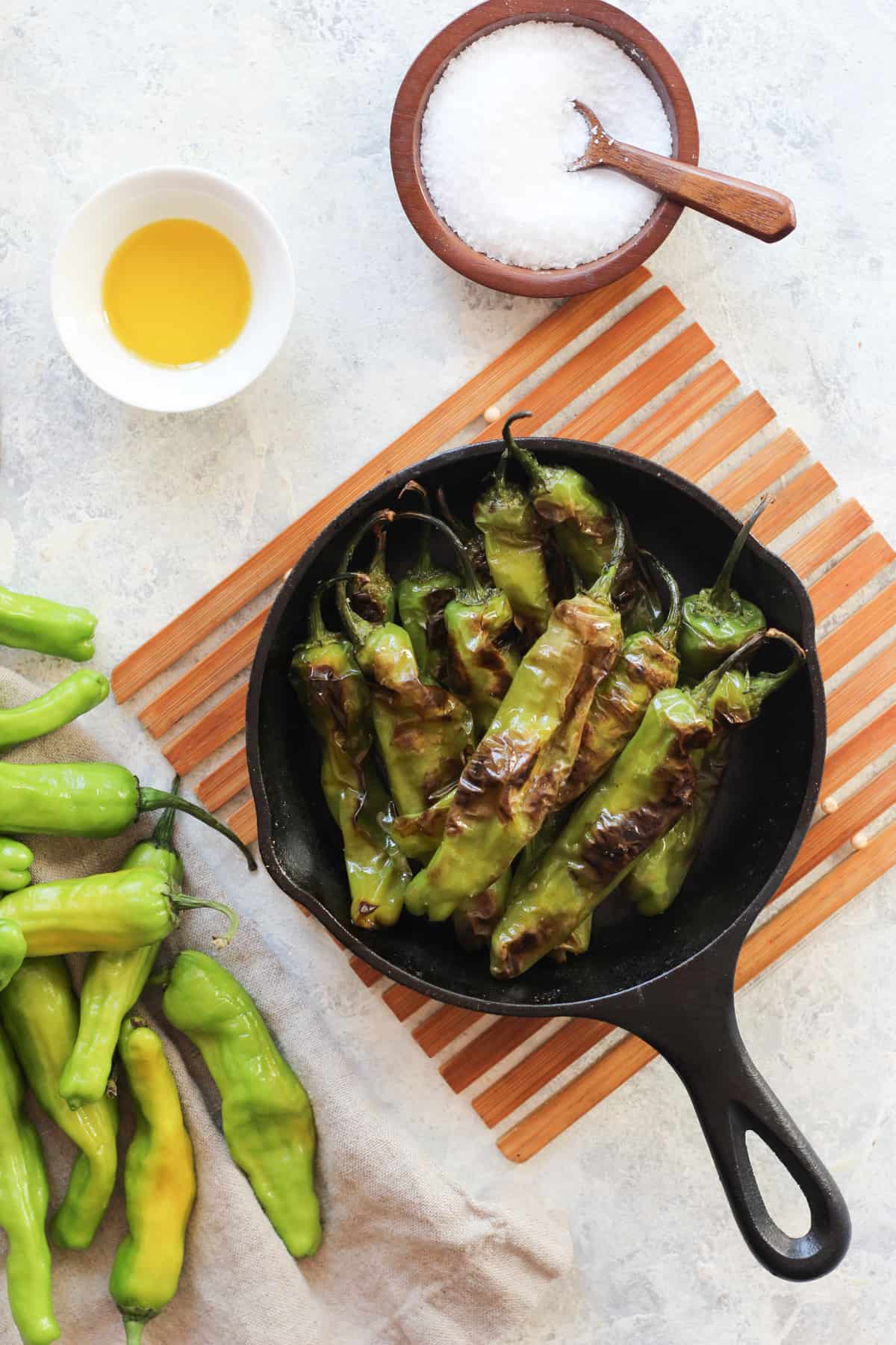 Blistered shishito peppers served in a cast iron next to fresh ones. 