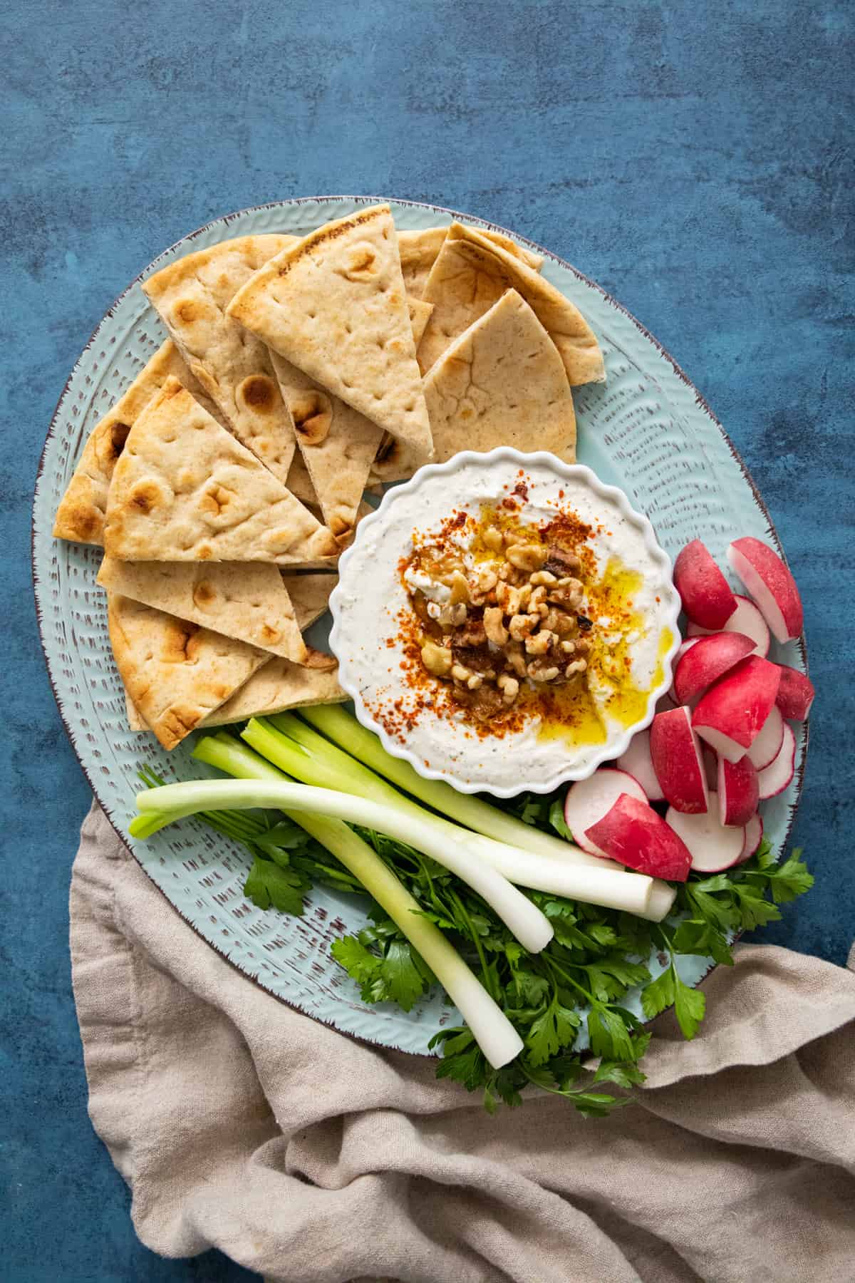 dip with feta in a bowl topped with walnuts on a blue platter.