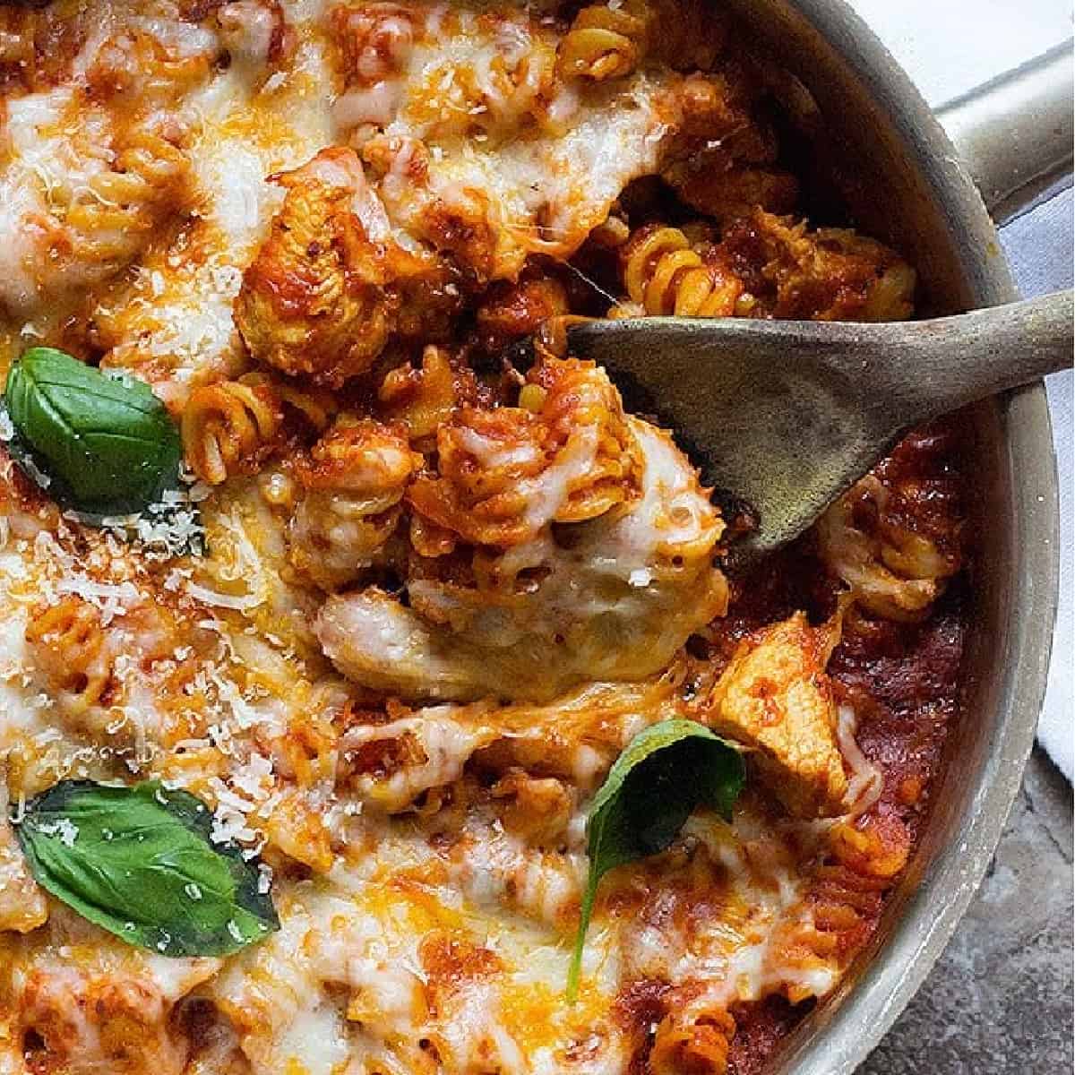 A wooden spoon scooping pasta out of pan. 