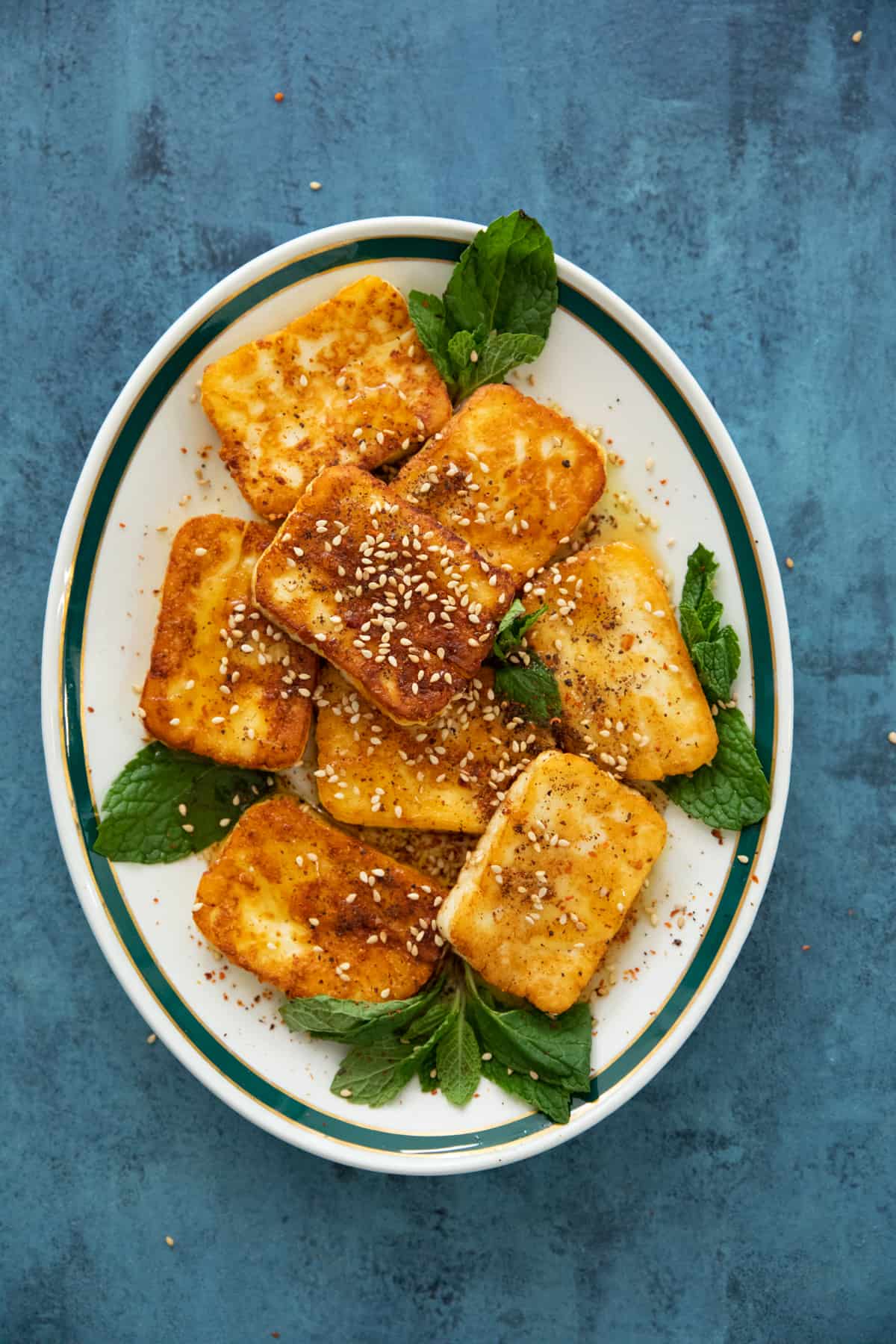 Pan fried halloumi on a white plate drizzled with honey and sesame seeds. 