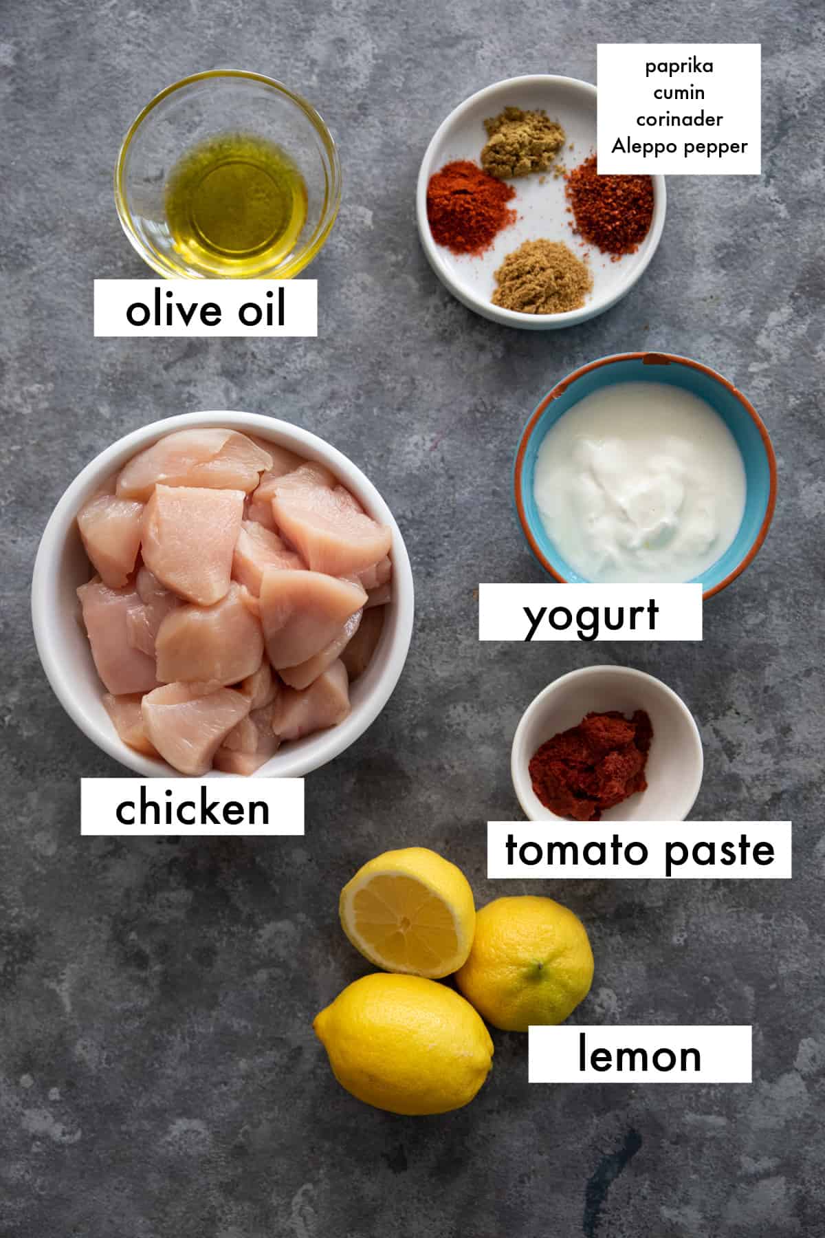 chicken, olive oil, spices, yogurt, tomato paste, lemon juice on a grey backdrop. 