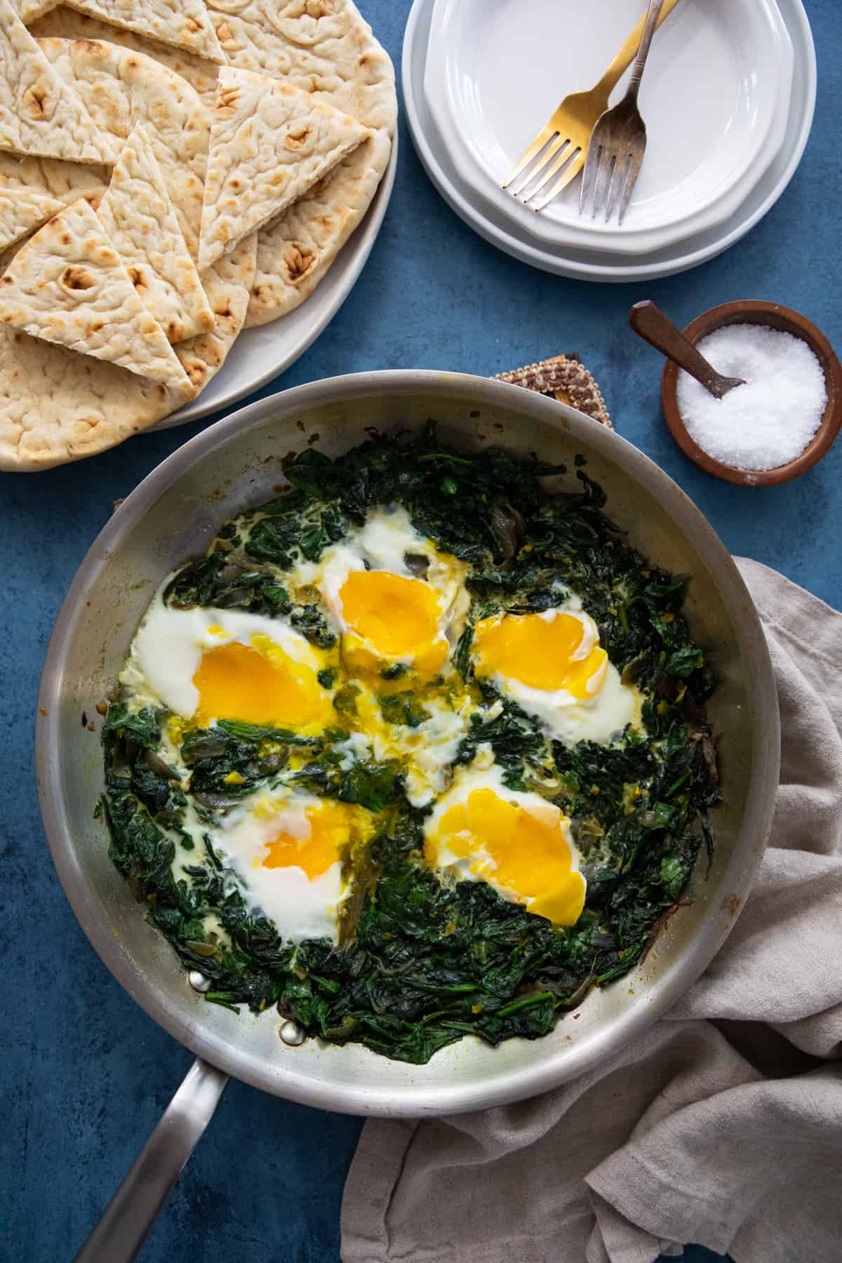 spinach and eggs in a pan on a blue backdrop. 