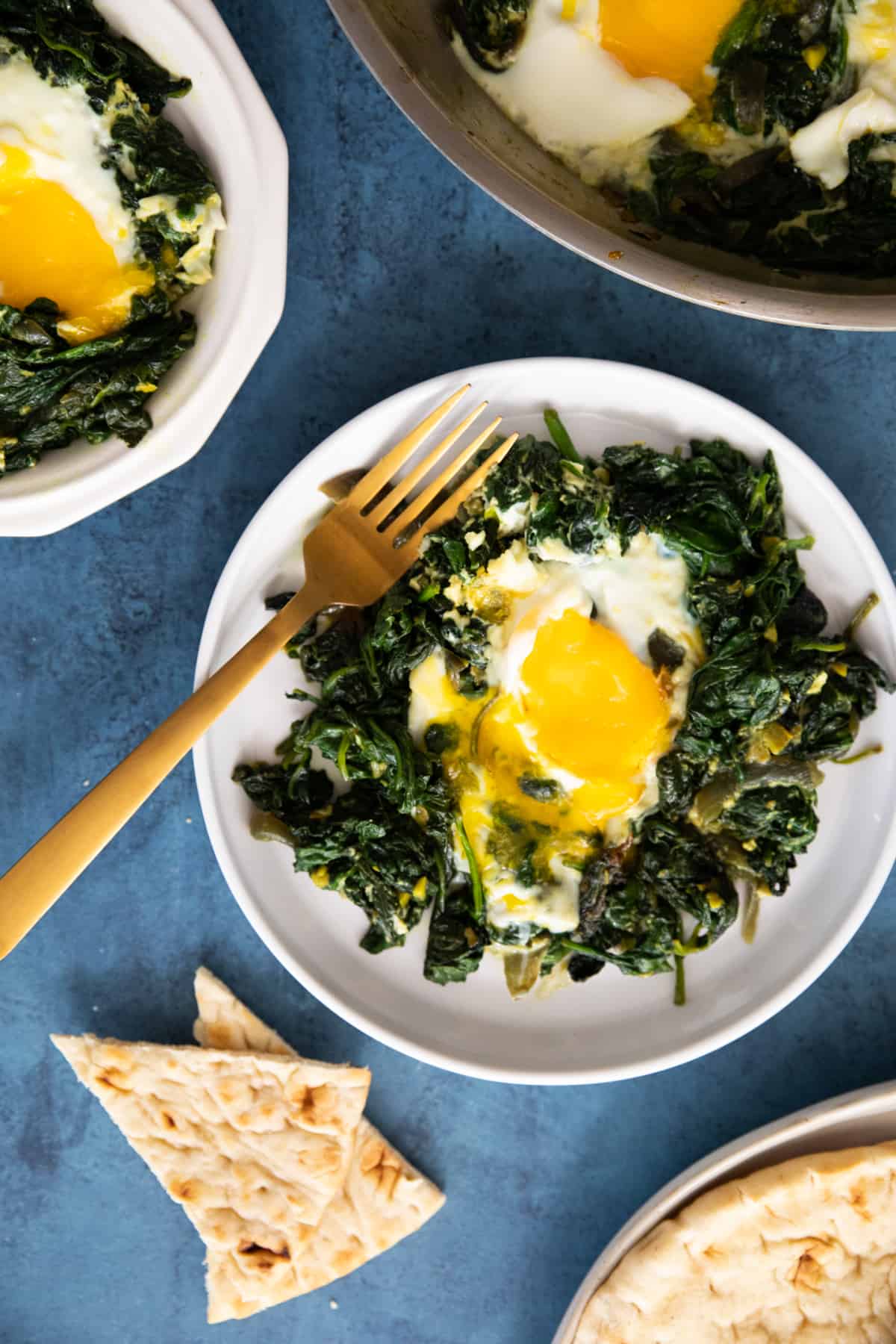 spinach and eggs on 2 plates on a blue backdrop.