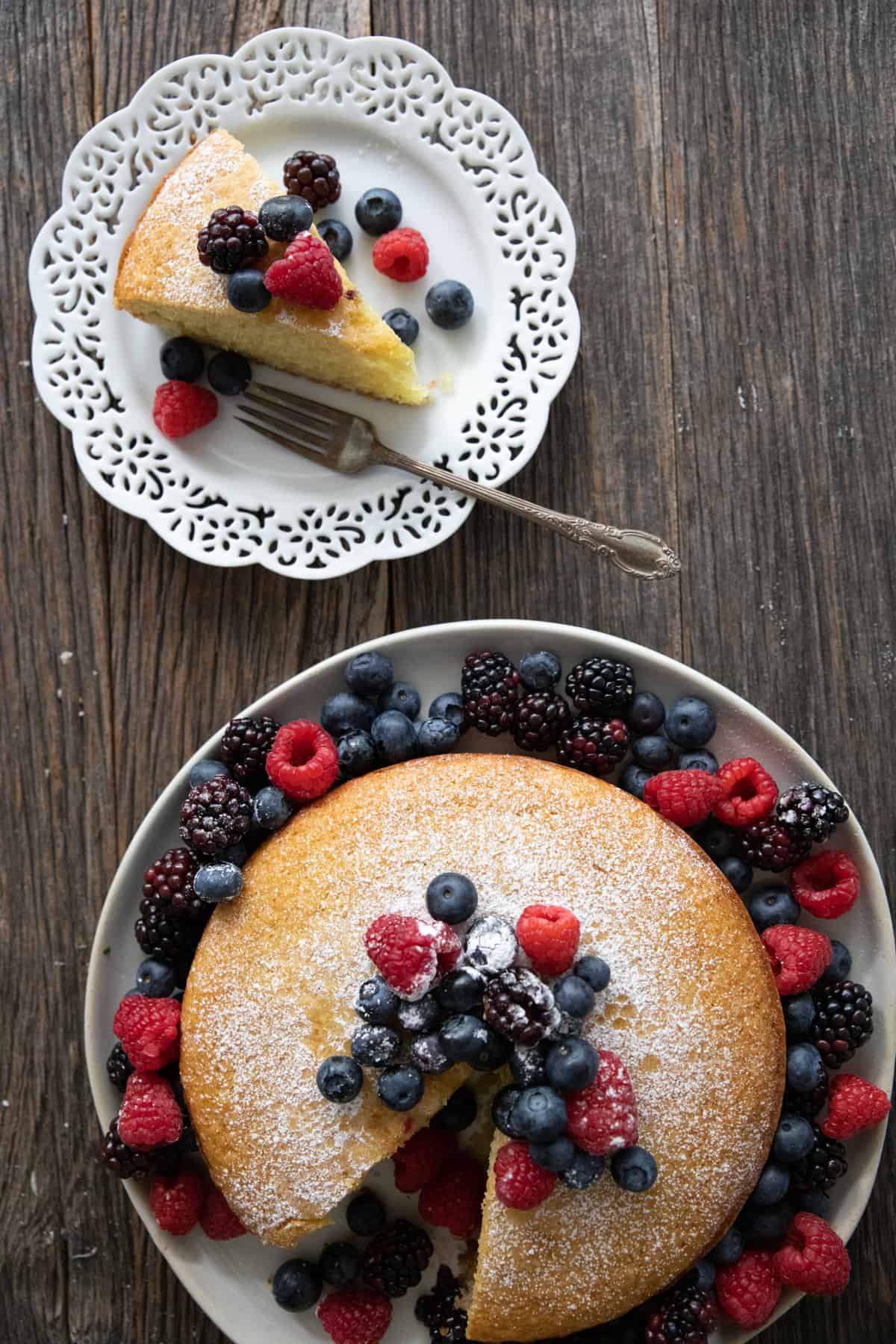 a slice of olive oil cake on a plate and the rest of the cake on a large plate .