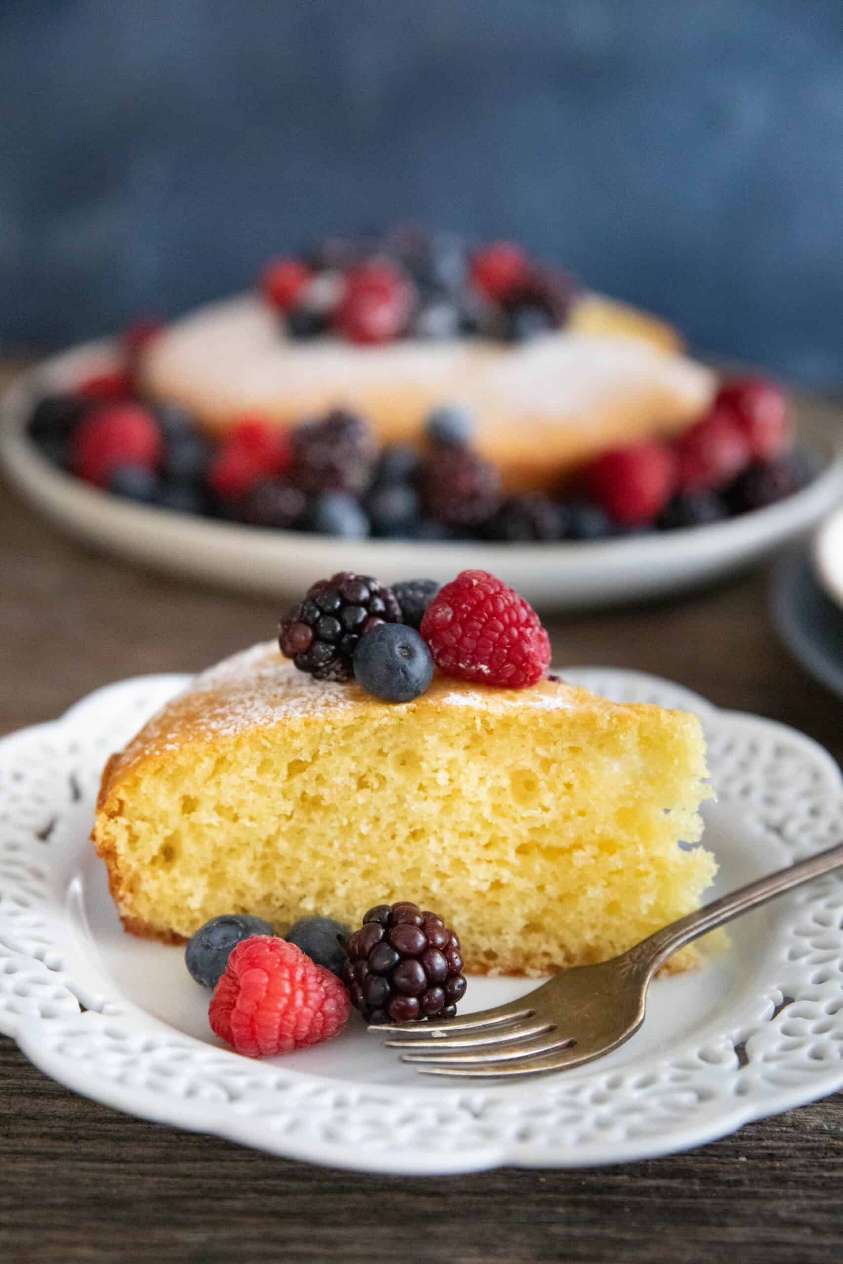 A slice on cake on a white plate on a wooden backdrop.