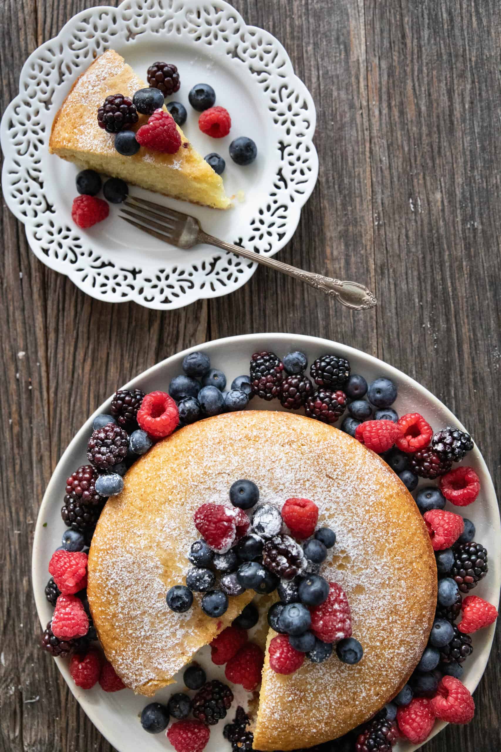 a slice of olive oil cake on a plate and the rest of the cake on a large plate .