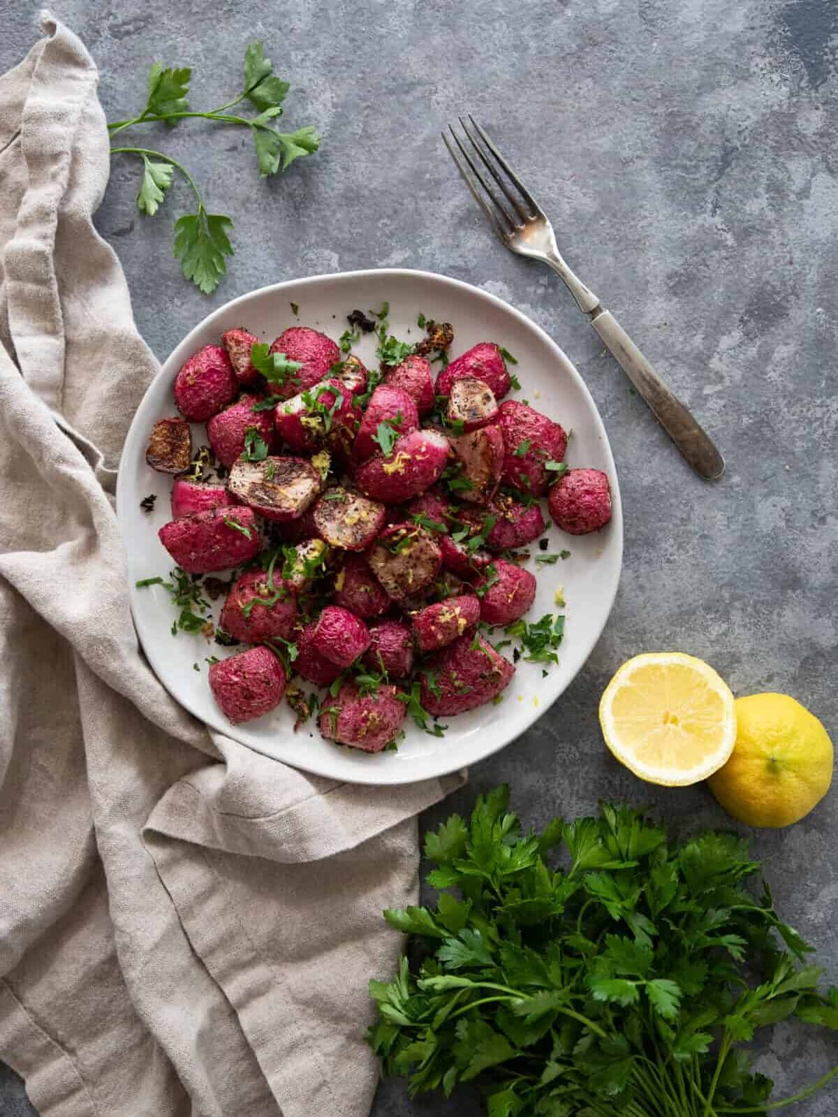overhead shot of red radishes on a plate with parsley and a linen napkin
