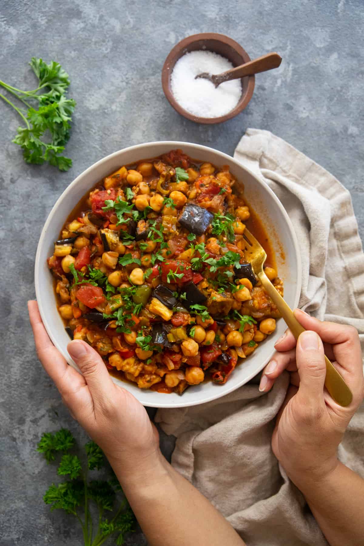 overhead shot of eggplant chickpea stew with hand serving it. 