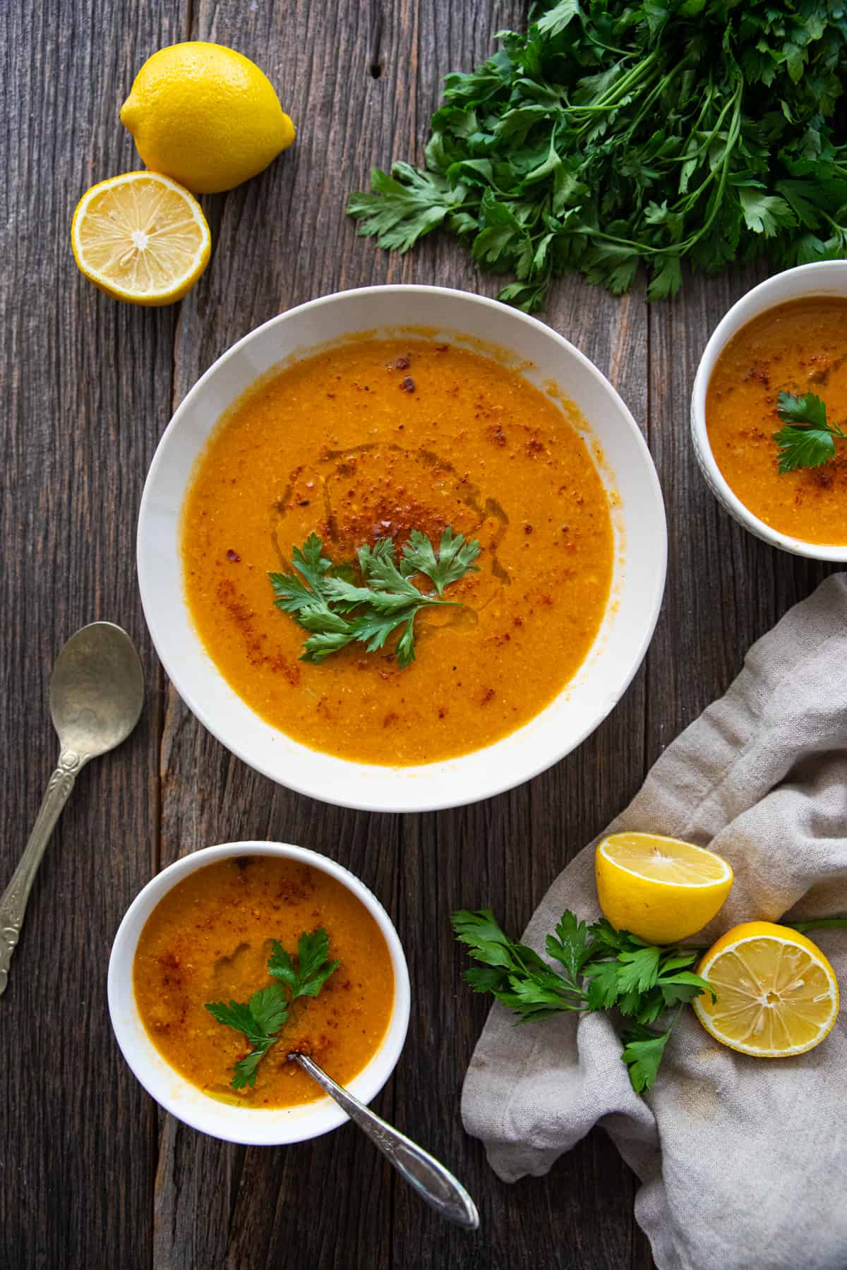 three bowls of red lentil soup Moroccan style on a table with a linen napkin and lemons. 