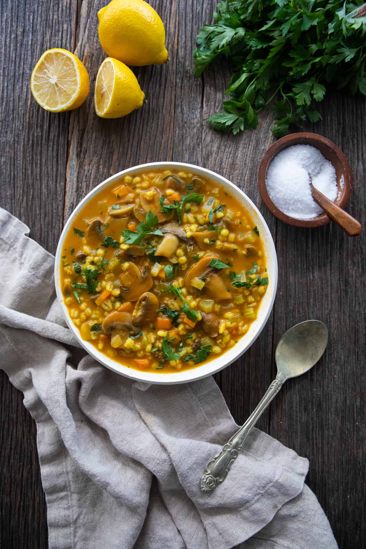 a bowl of mushroom barley soup on the table with lemon and parsley. 