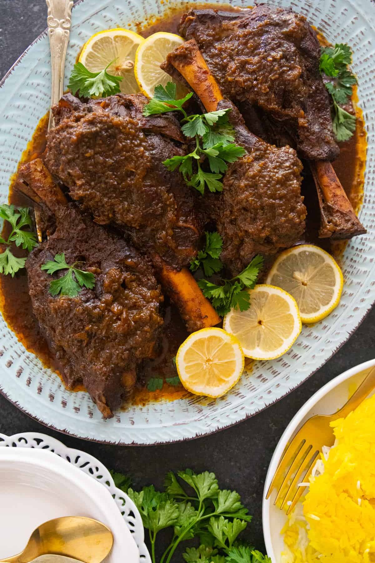 braised lamb shanks served on a platter with herbs and lemon.