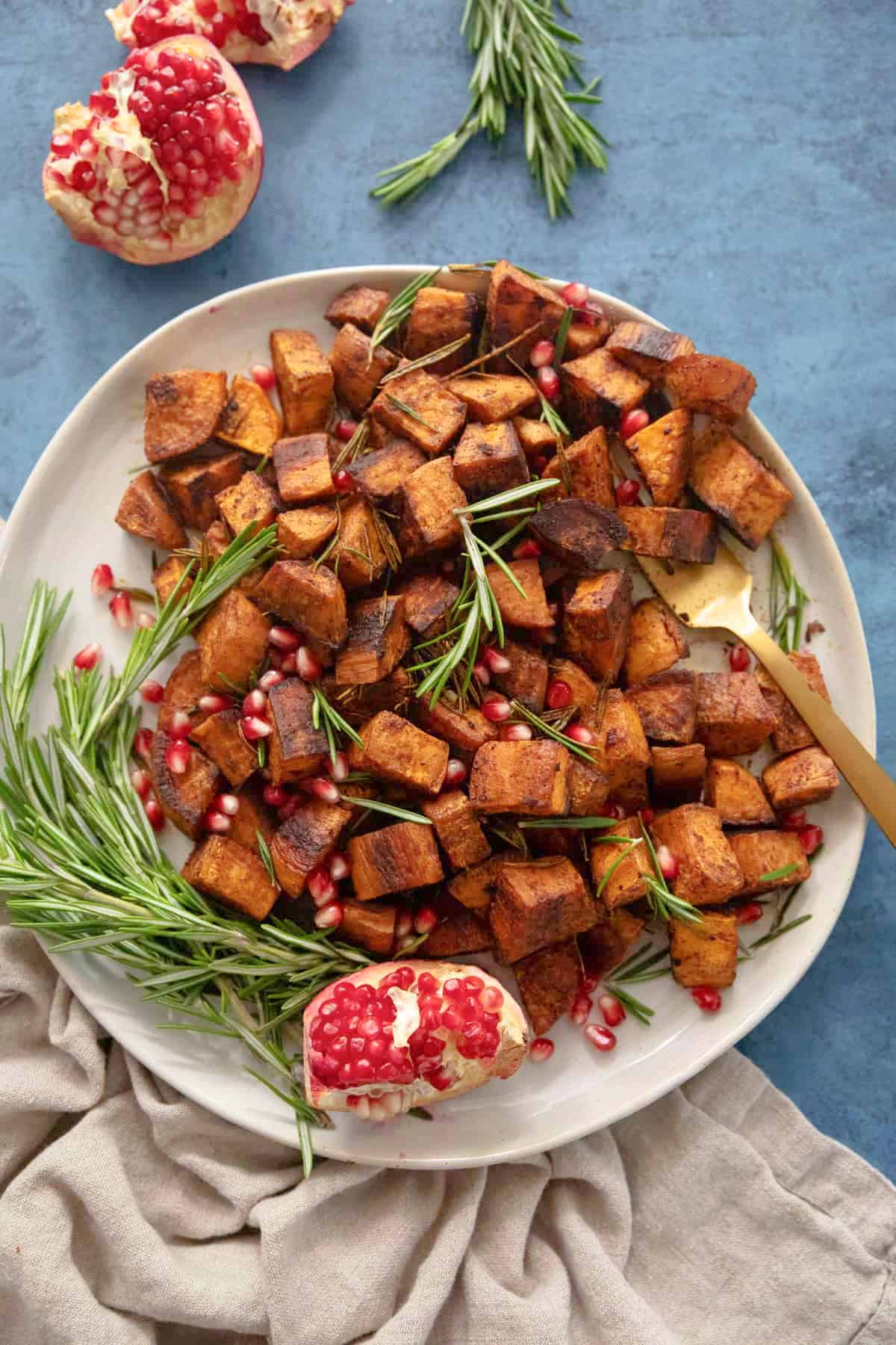 a plate of roasted sweet potatoes with roasemary and pomegranate on a blue backdrop. 