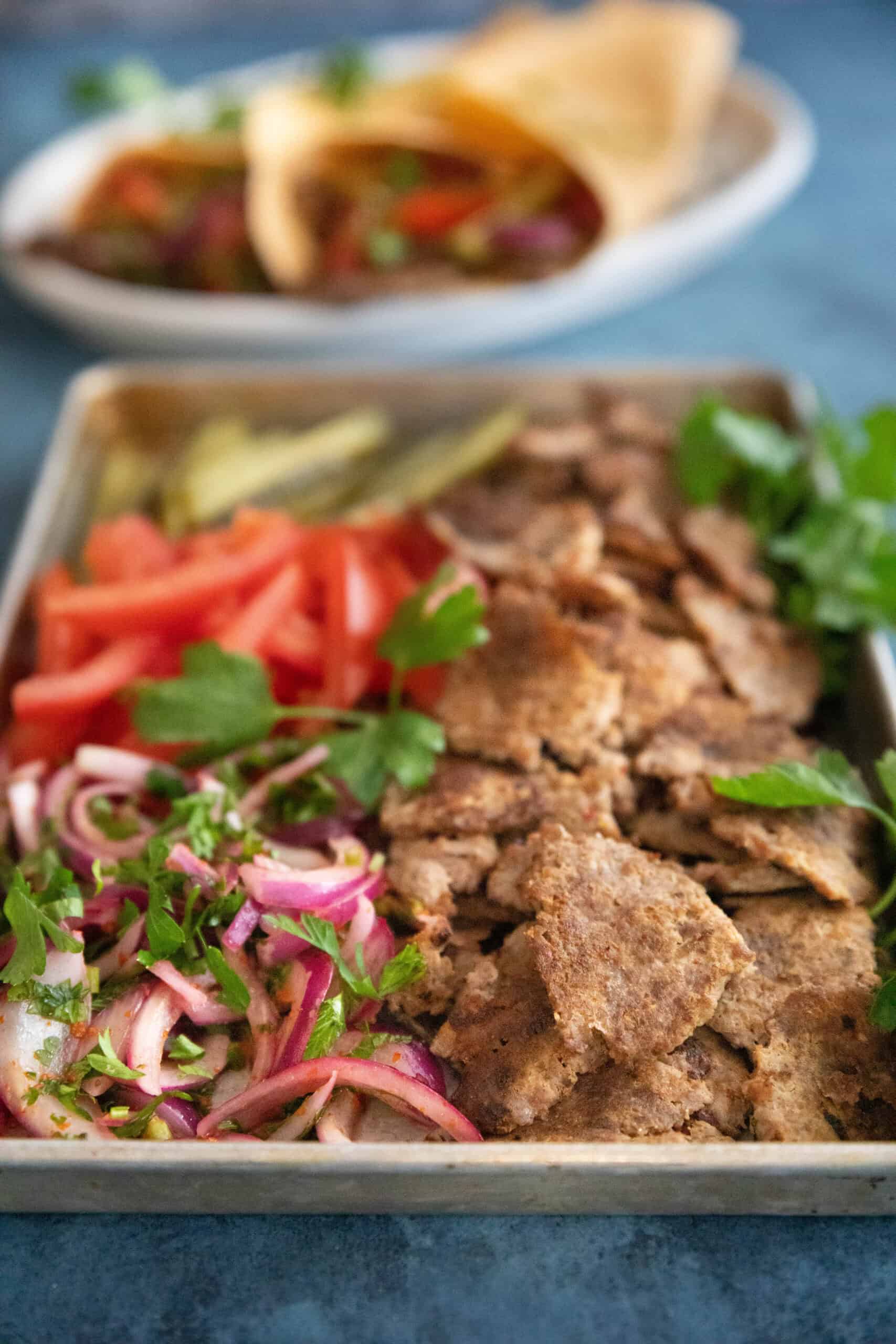 beef doner on a baking sheet with tomatoes and pickles and sumac onion. 