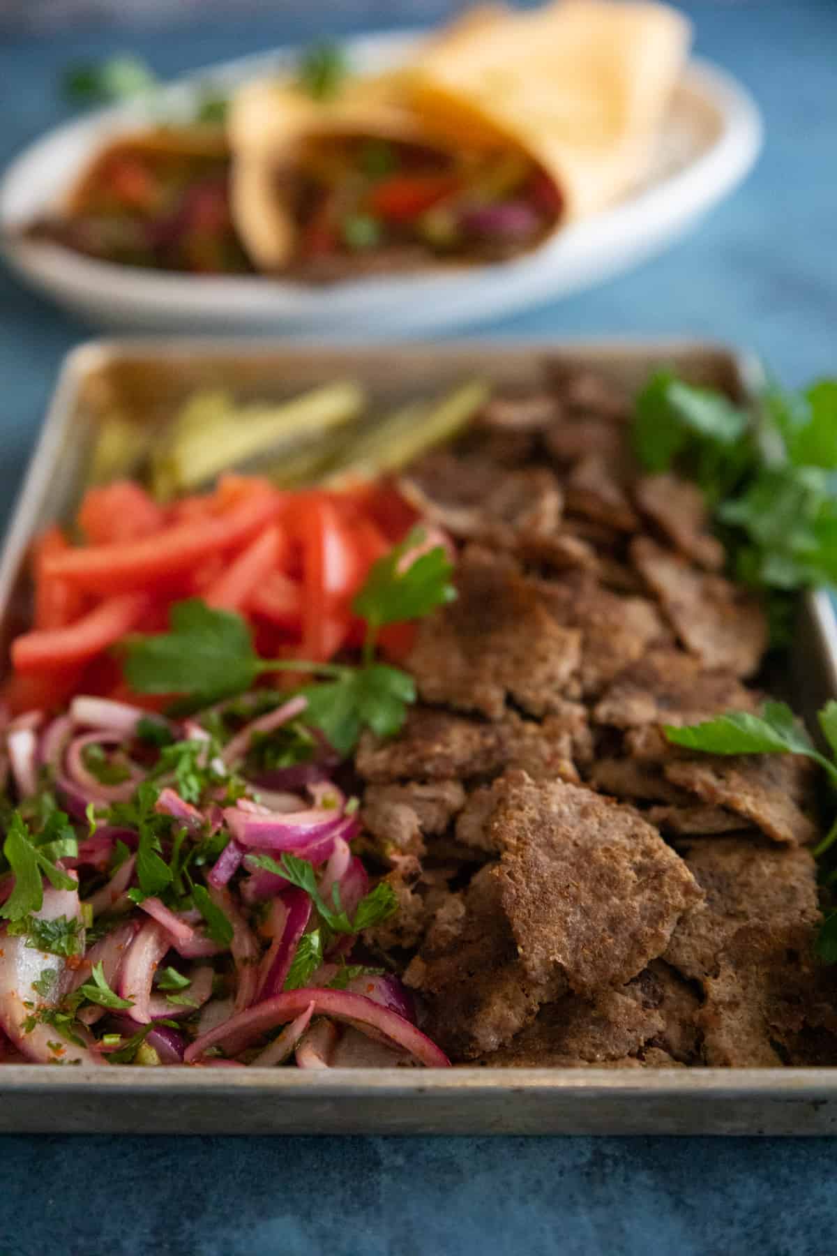 beef doner on a baking sheet with tomatoes and pickles and sumac onion. 