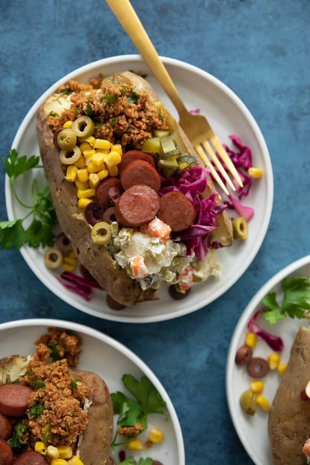 overhead shot of kumpir Turkish stuffed baked potatoes with hotdogs, kisir, olives and Russian salad.