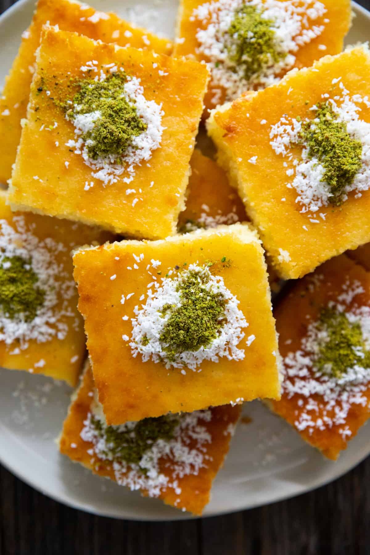 a few slices of revani cake on a plate topped with coconut and pistachio. 