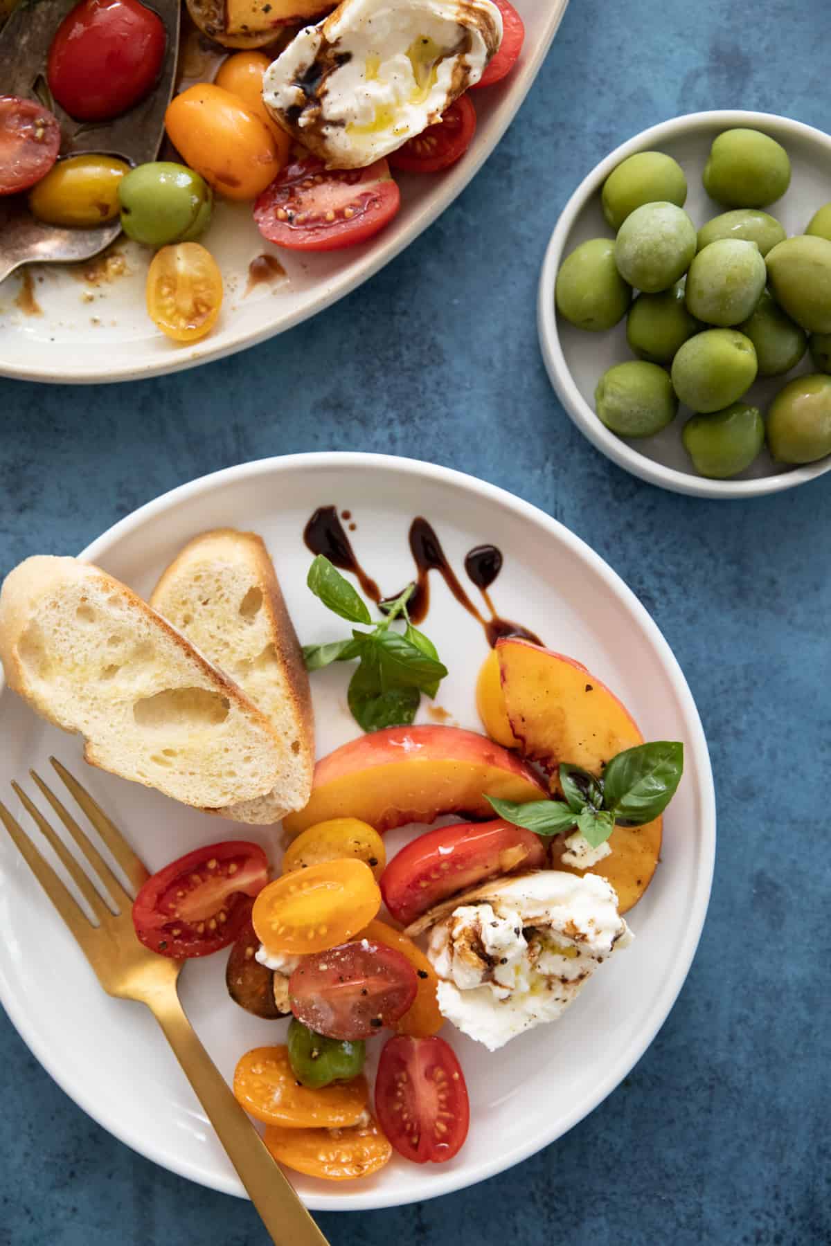 Burrata on a plate with balsamic glaze and fruit and bread. 