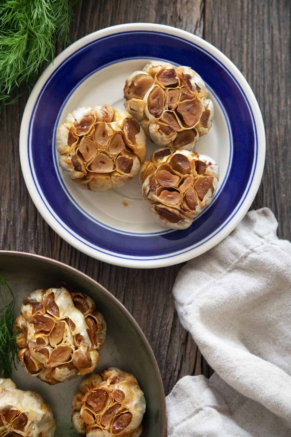 three roasted whole garlics on a blue plate.