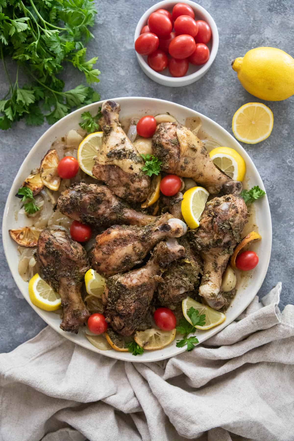 Cooked chicken legs on a plate with tomatoes and lemon. 