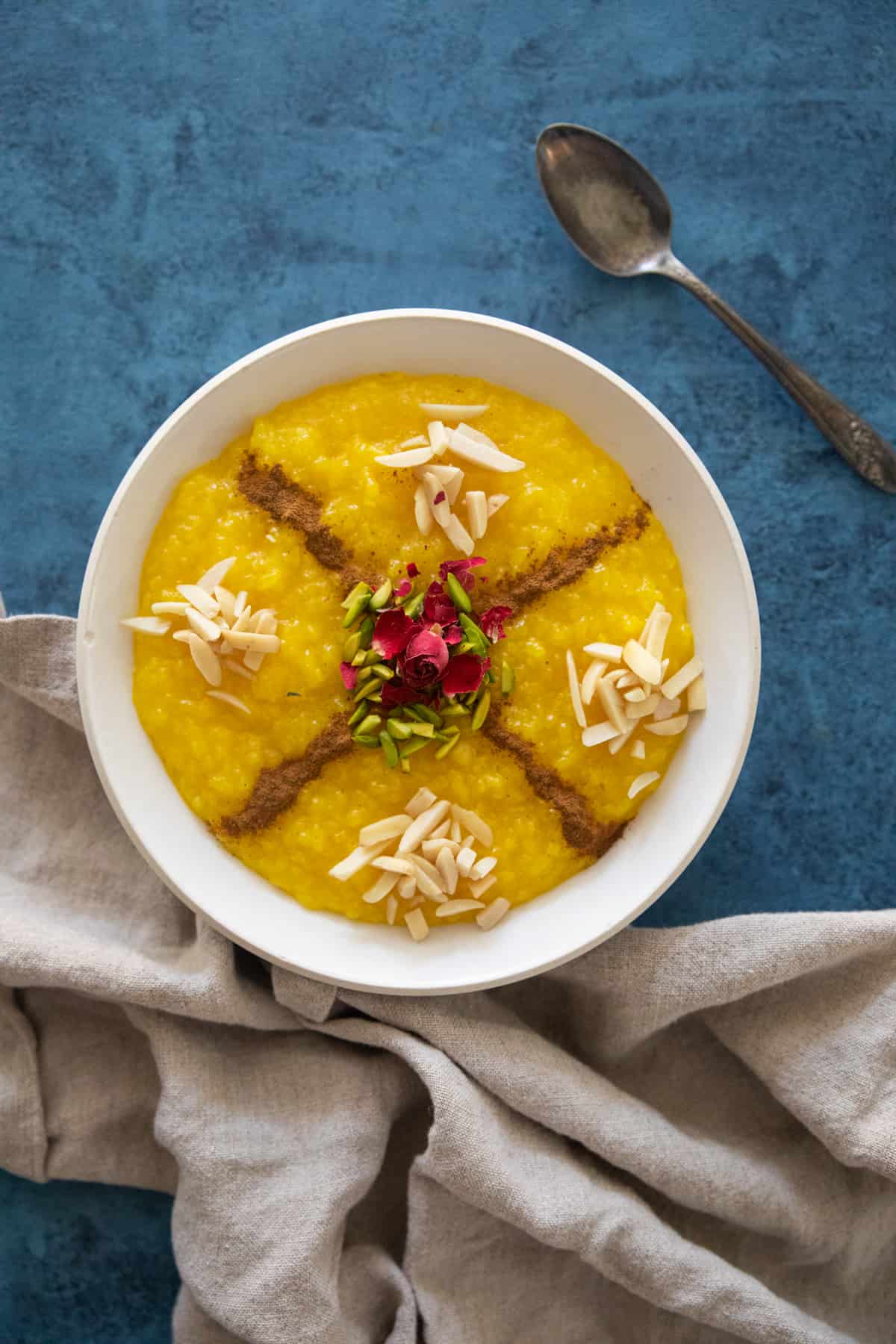 Sholeh zard Persian saffron rice pudding in a bowl on a blue backdrop. 