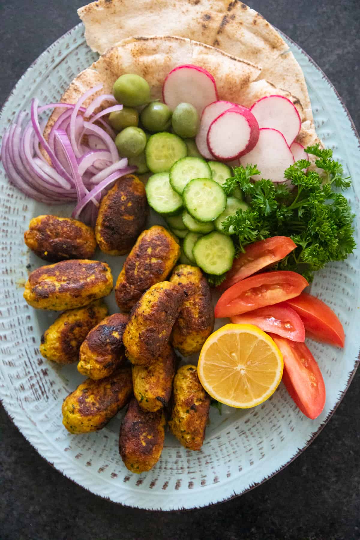 Chicken kofta on a platter with bread and vegetables. 