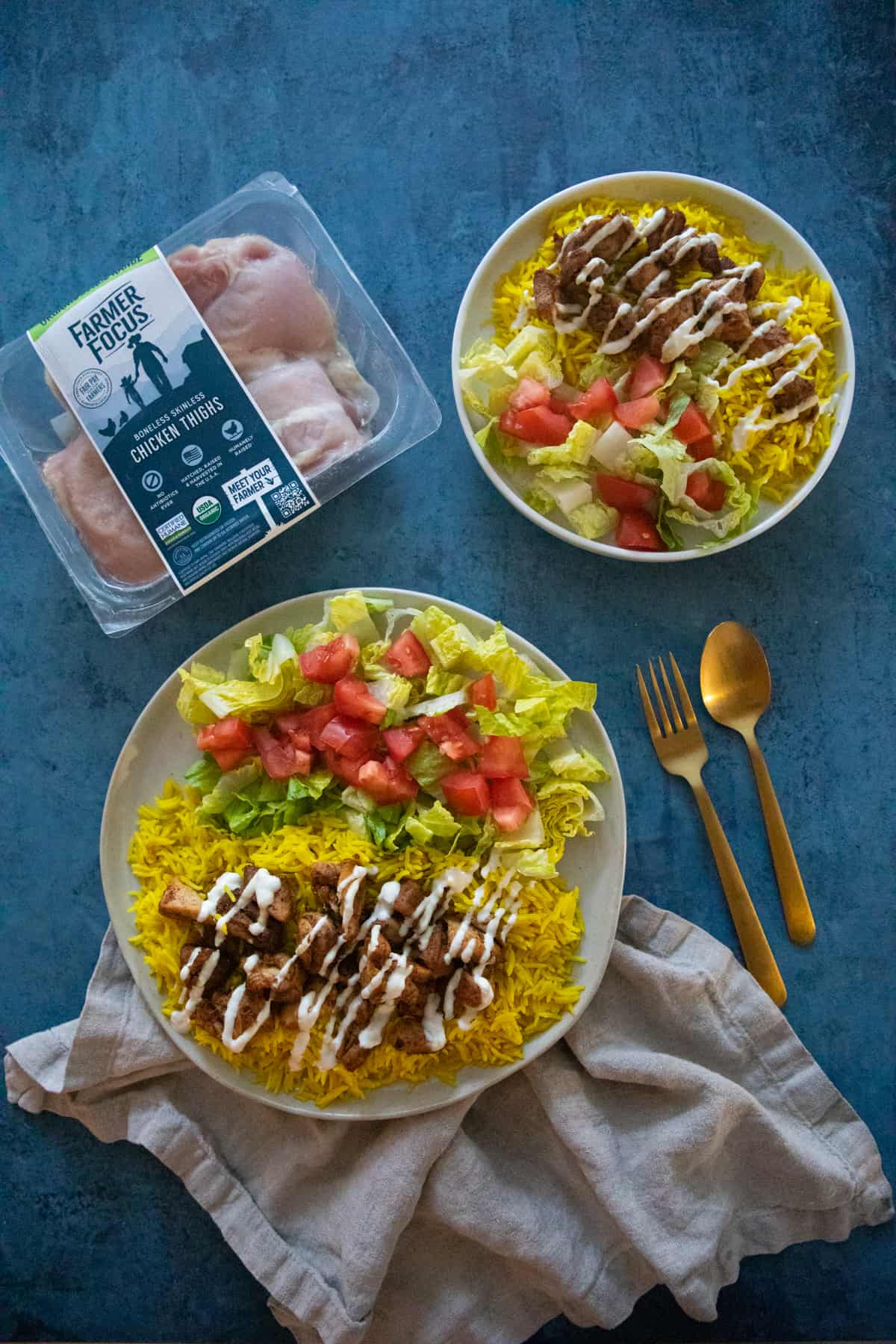 Two plates of chicken and rice on a blue backdrop. 