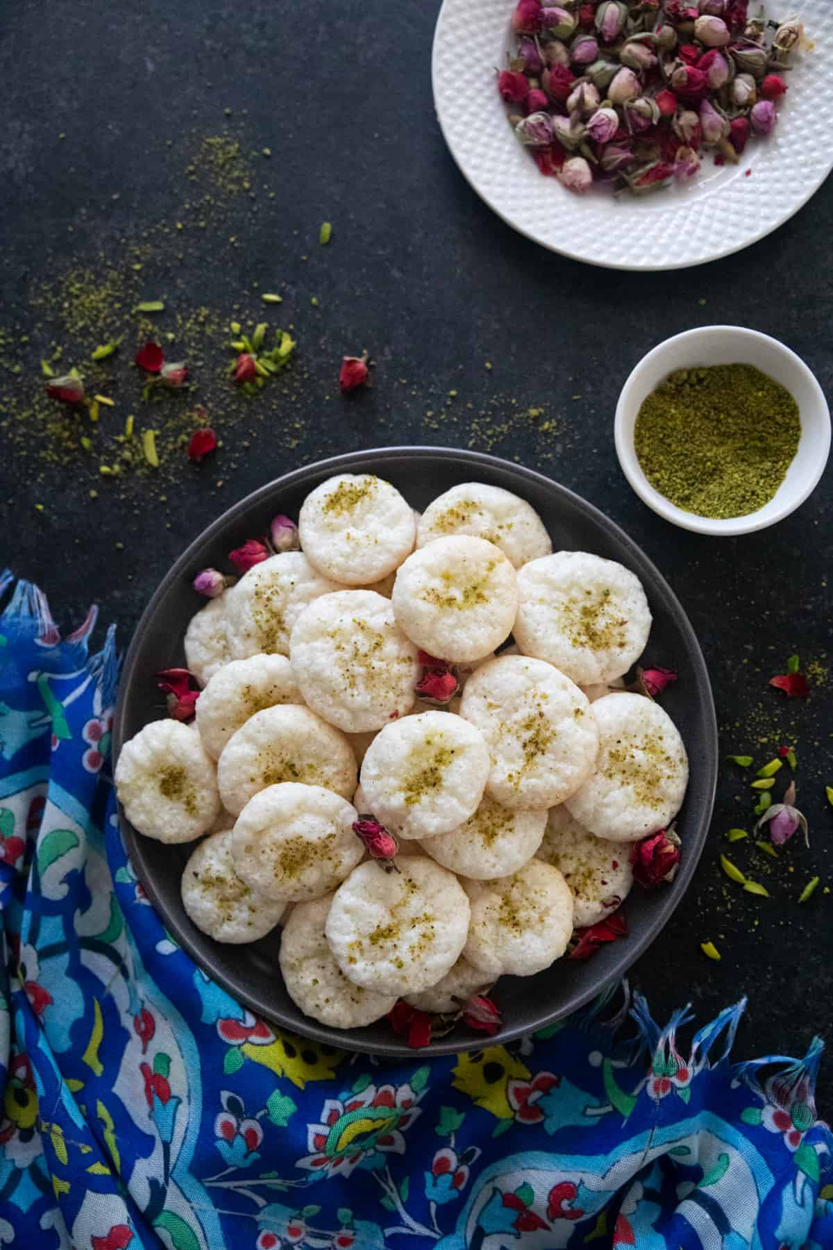 A plate of shirini nargili Persian coconut cookies on a dark backdrop. 