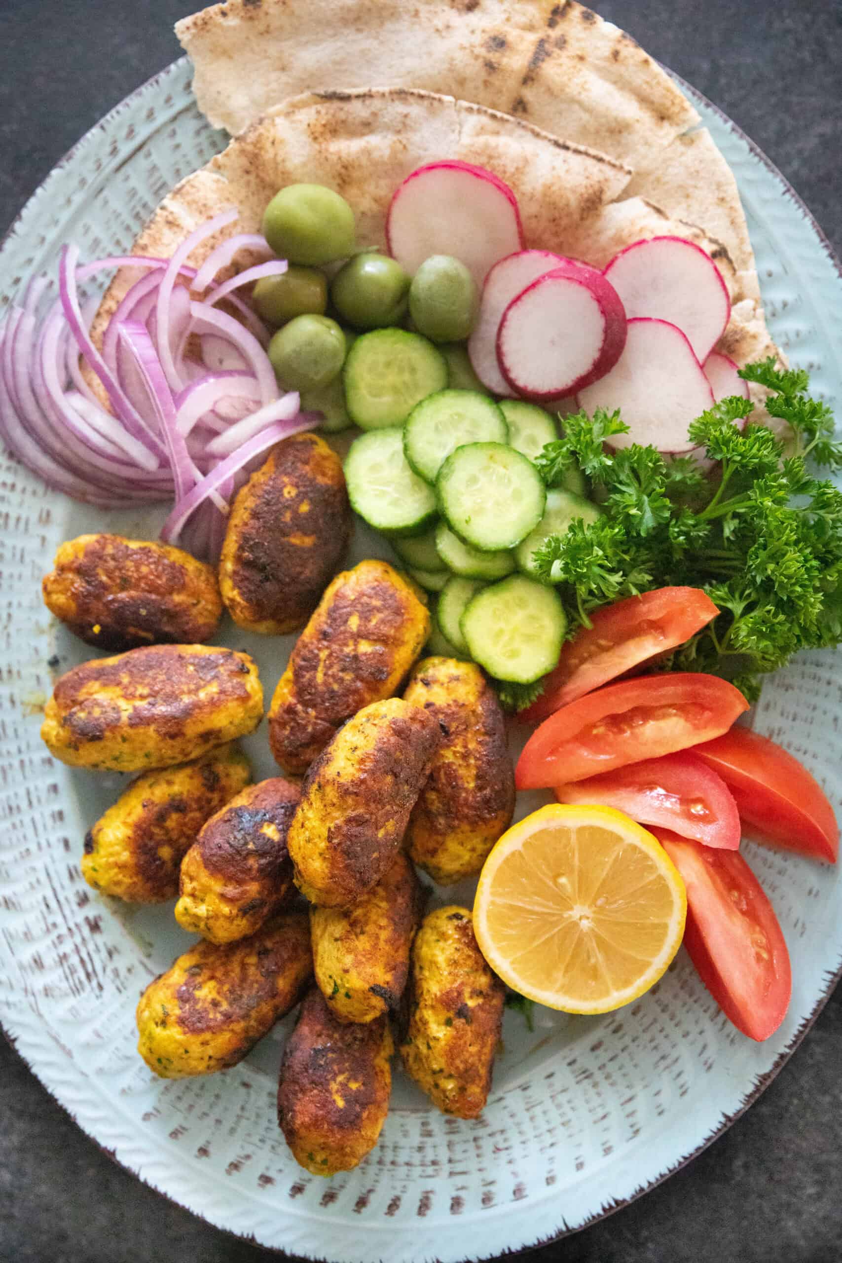 Chicken kofta on a platter with bread and vegetables. 