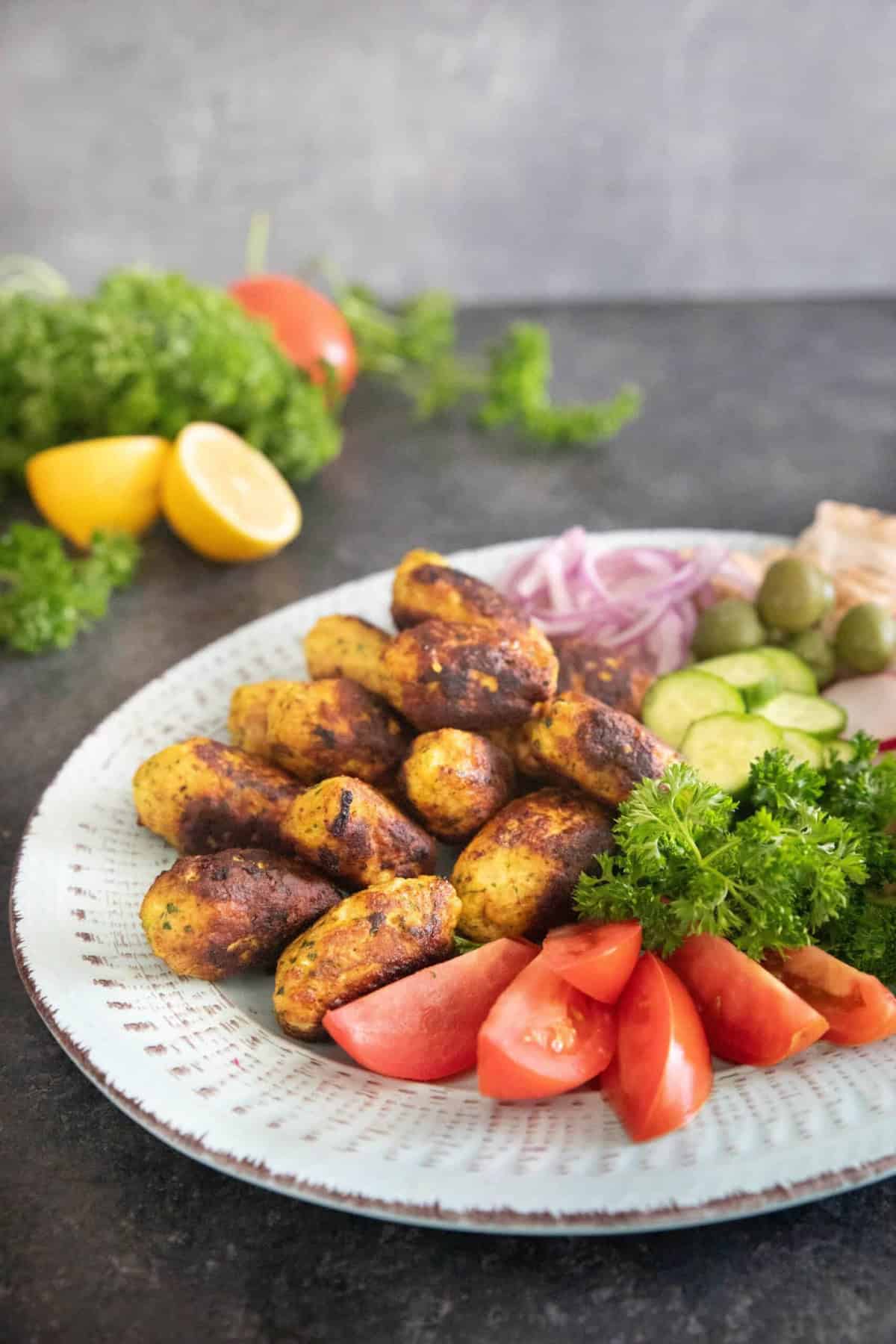 Chicken kofta on a platter with bread and vegetables. 