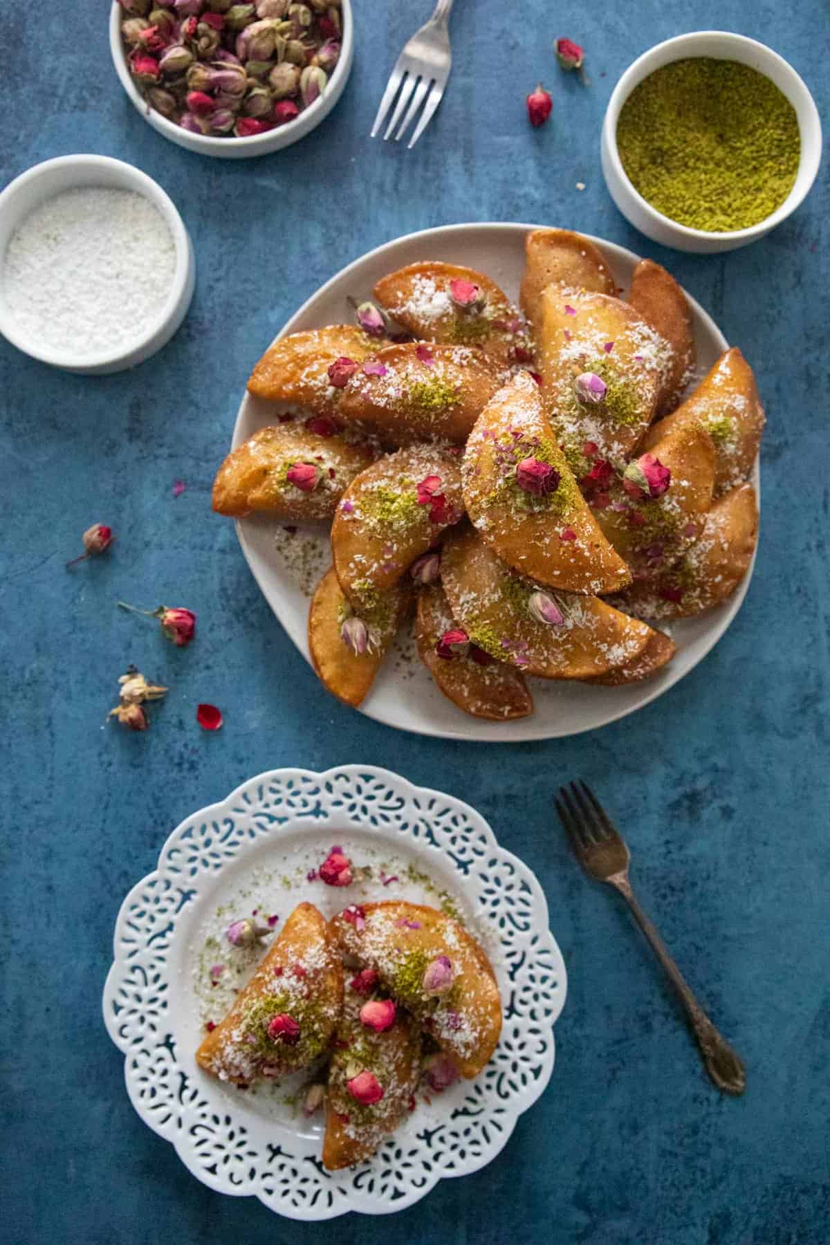 Two plates of qatayef on a blue backdrop. 