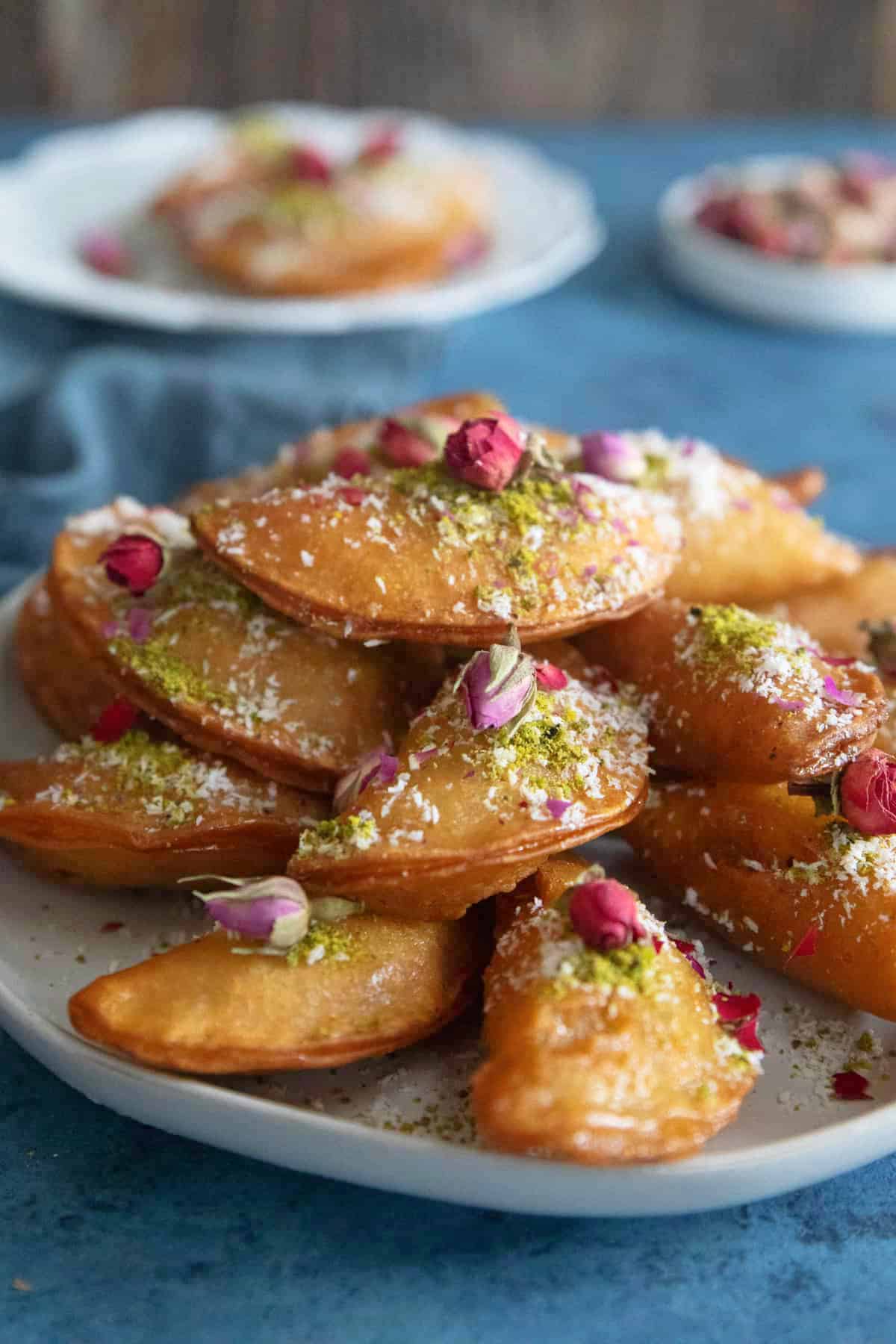 Qatayef on a plate topped with pistachios and rose. 