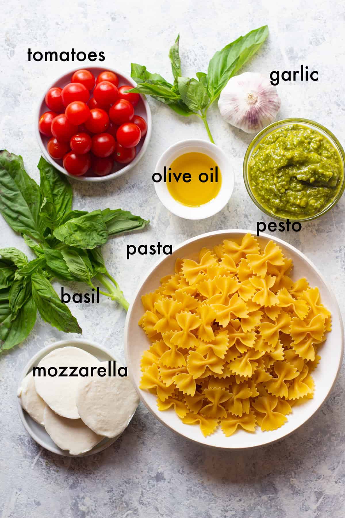 Caprese pasta salad ingredients: pasta, mozzarella, tomatoes, basil, olive oil, garlic, pesto.