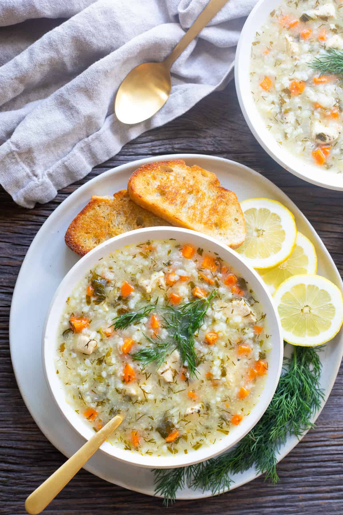 Overhead shot of chicken and rice soup in a bowl on a plate with bread and lemon. 