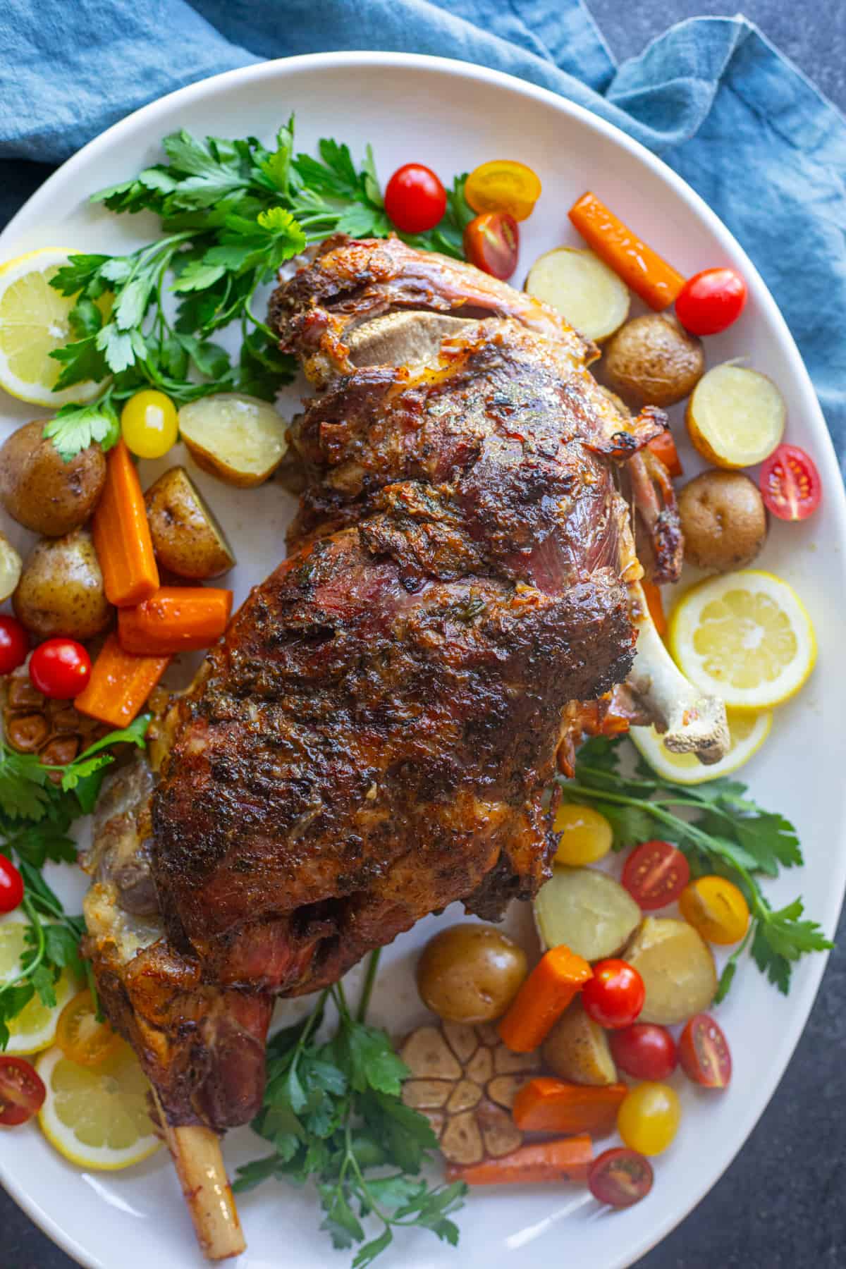 Slow roasted leg of lamb on a platter with vegetables.